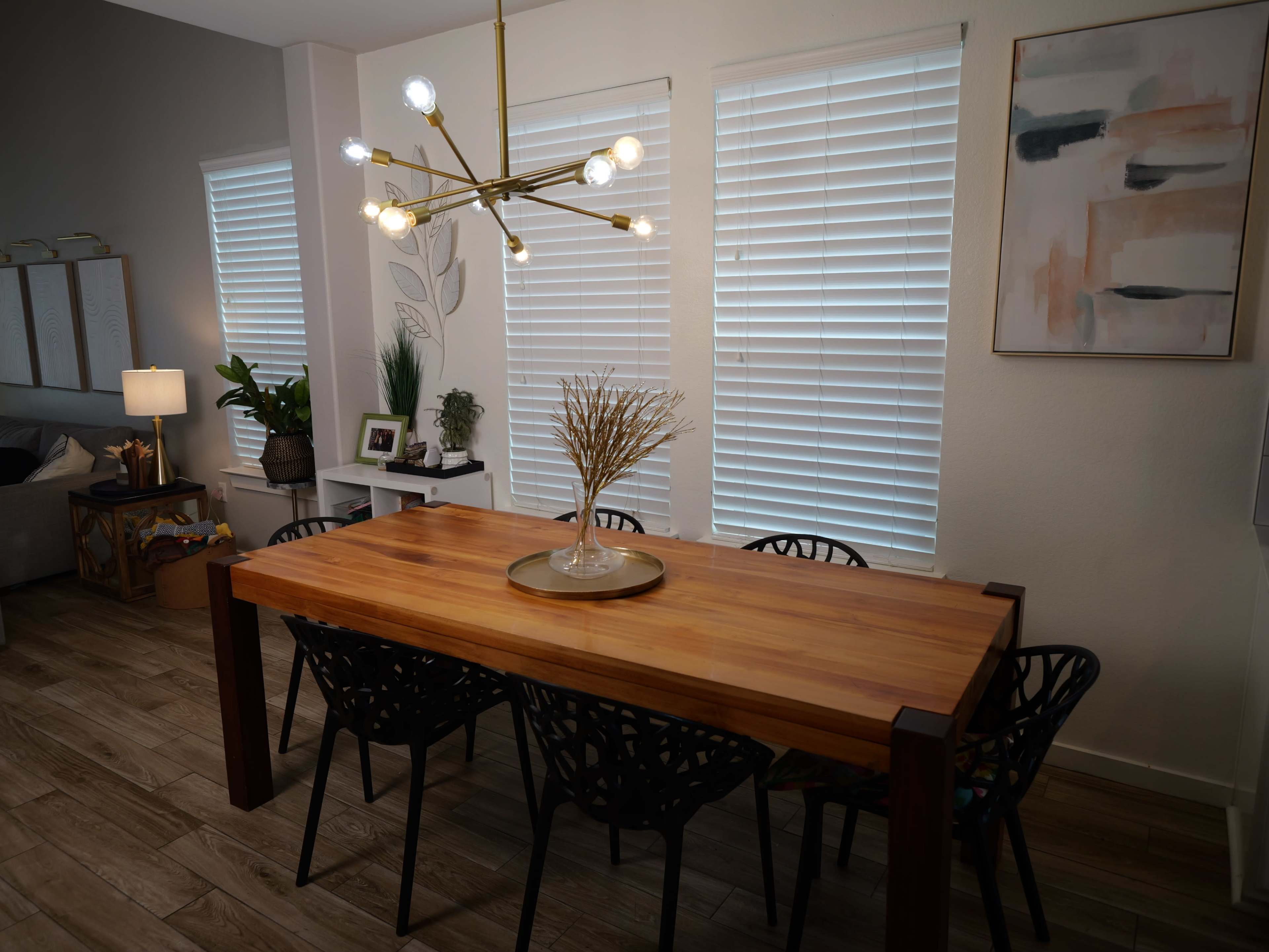 A wooden dining table surrounded by black chairs sits in a room with large windows and modern decor.