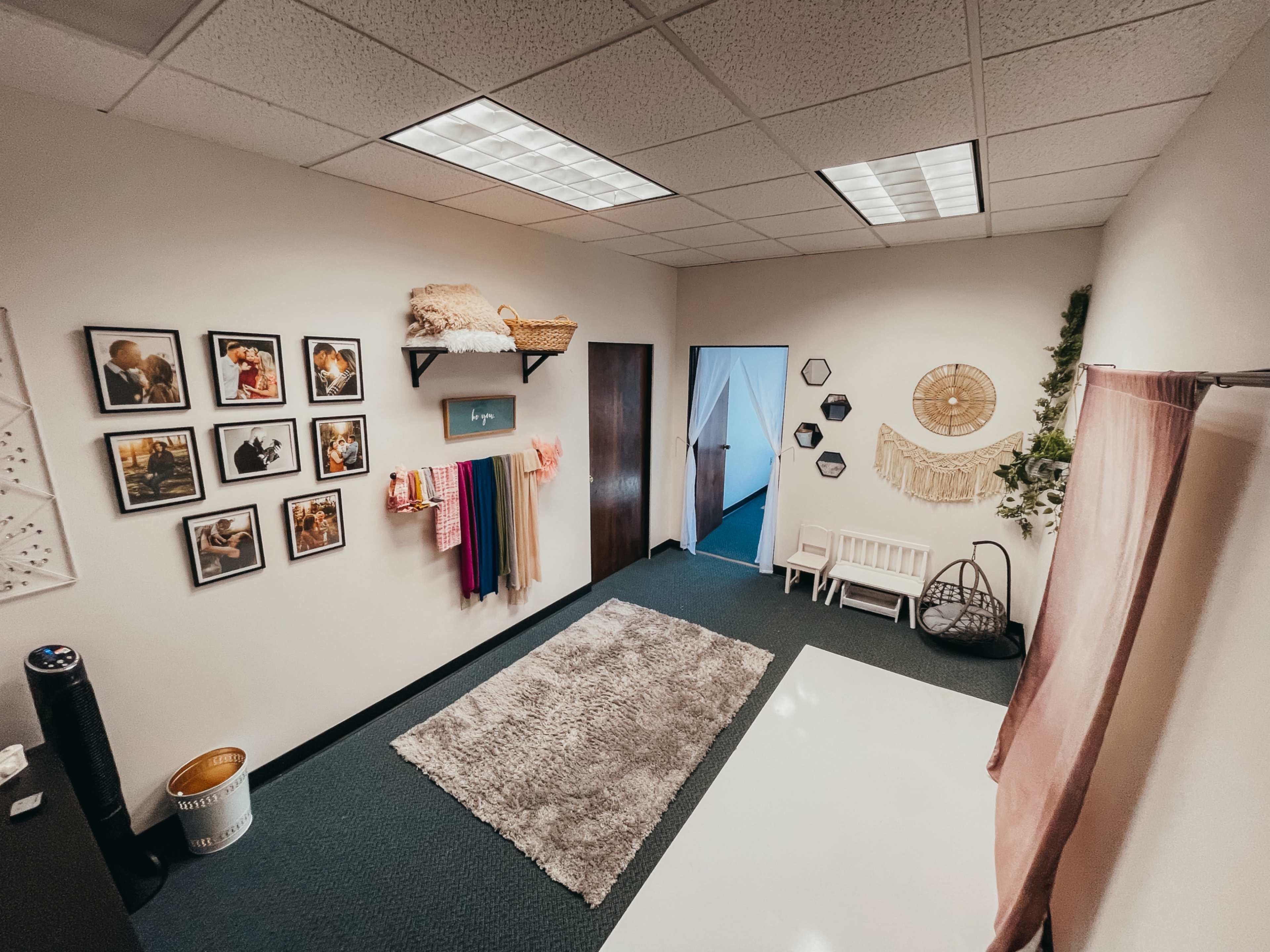 The image shows a well-organized interior space featuring framed photographs on the wall, a variety of colorful drapes, a cozy seating area, and decorative wall hangings.