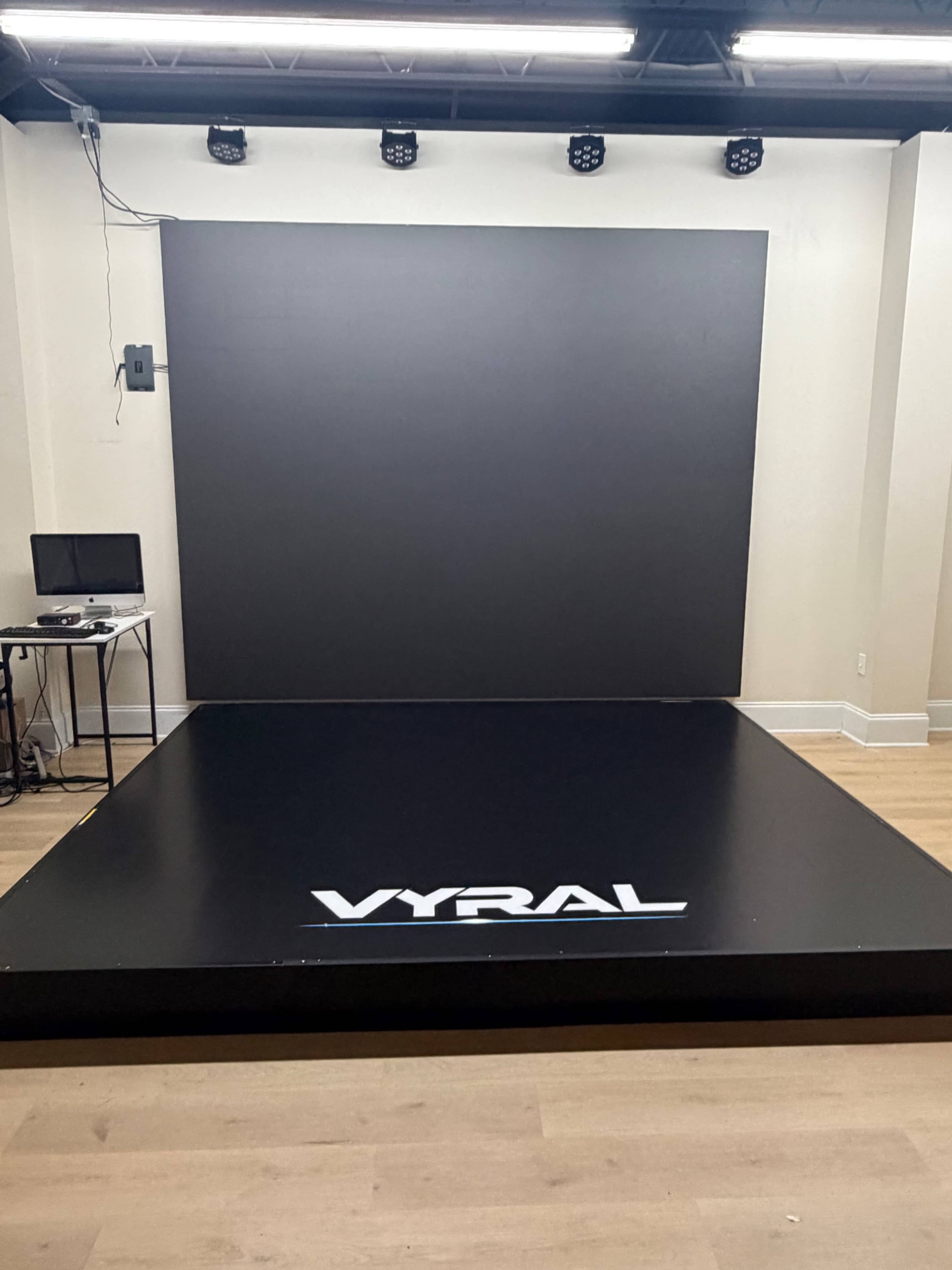 The image shows a black stage platform with the word "VYRAL" displayed prominently, set against a plain wall in a well-lit room.