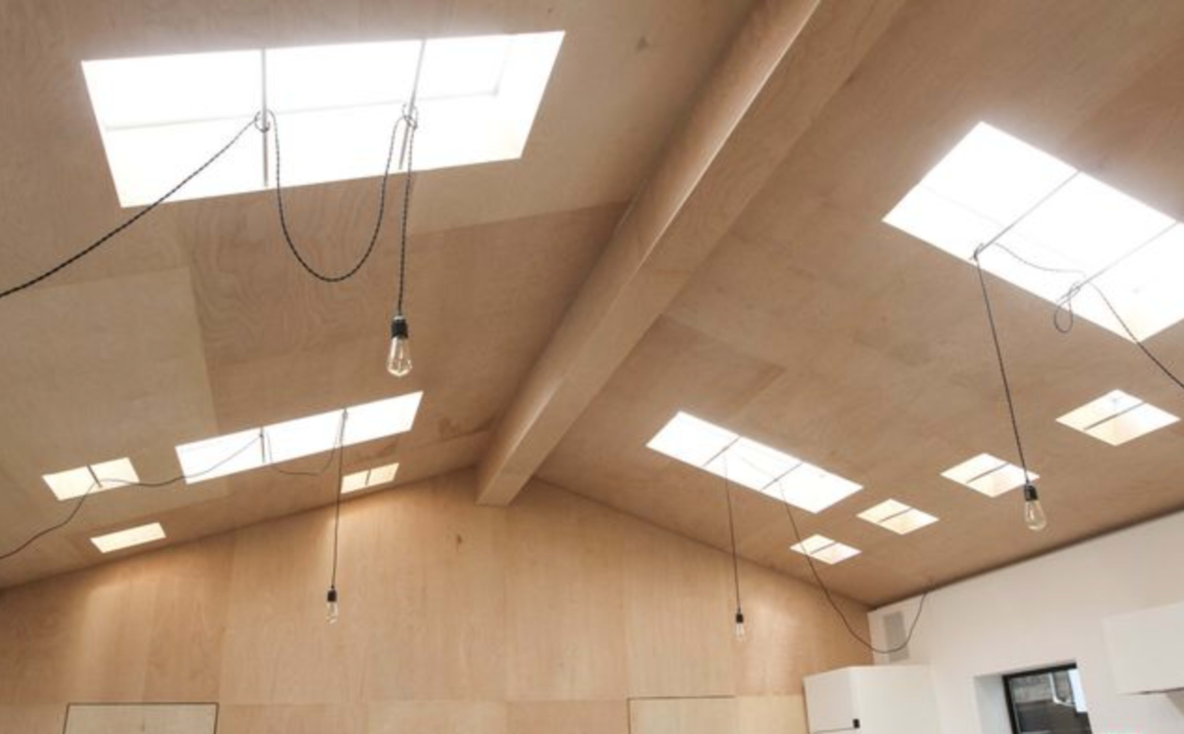 The image shows a ceiling featuring multiple skylights and hanging light bulbs in a wooden interior space.