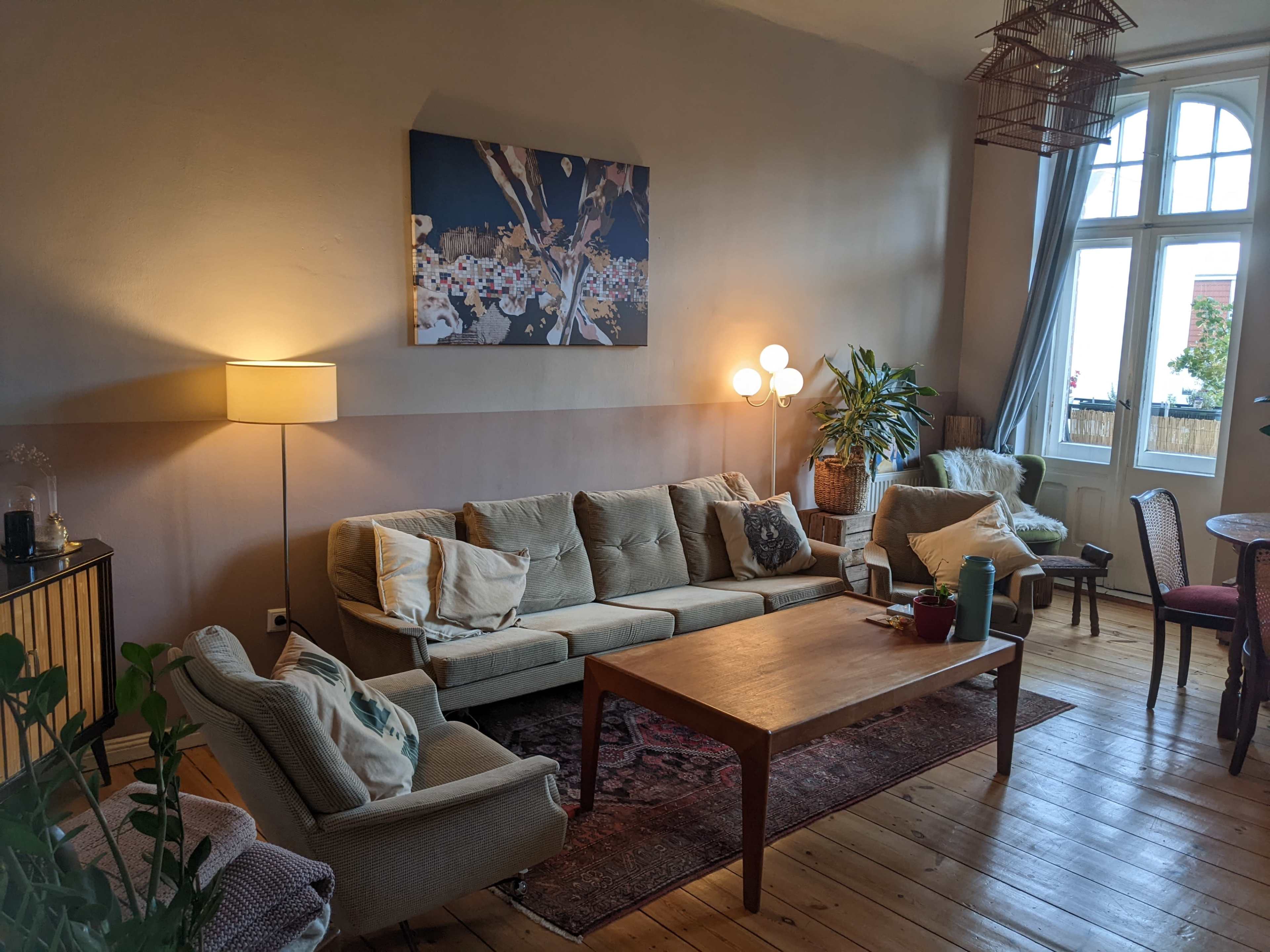 The living room features a large beige sectional sofa, a wooden coffee table, and a tall window with natural light illuminating the space.