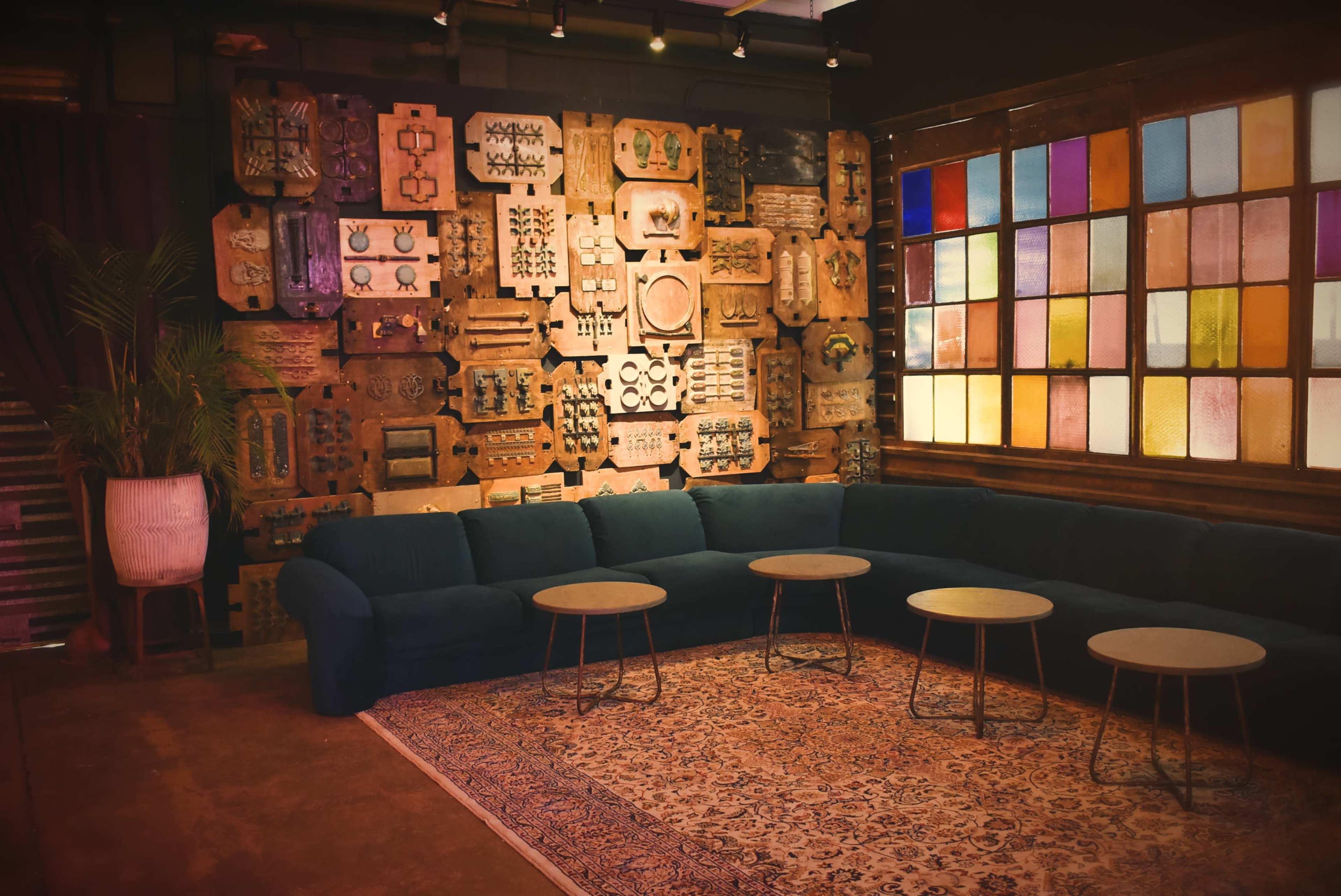 A cozy seating area features a blue sofa, several small tables, and a colorful stained glass window against a backdrop of patterned wooden panels.