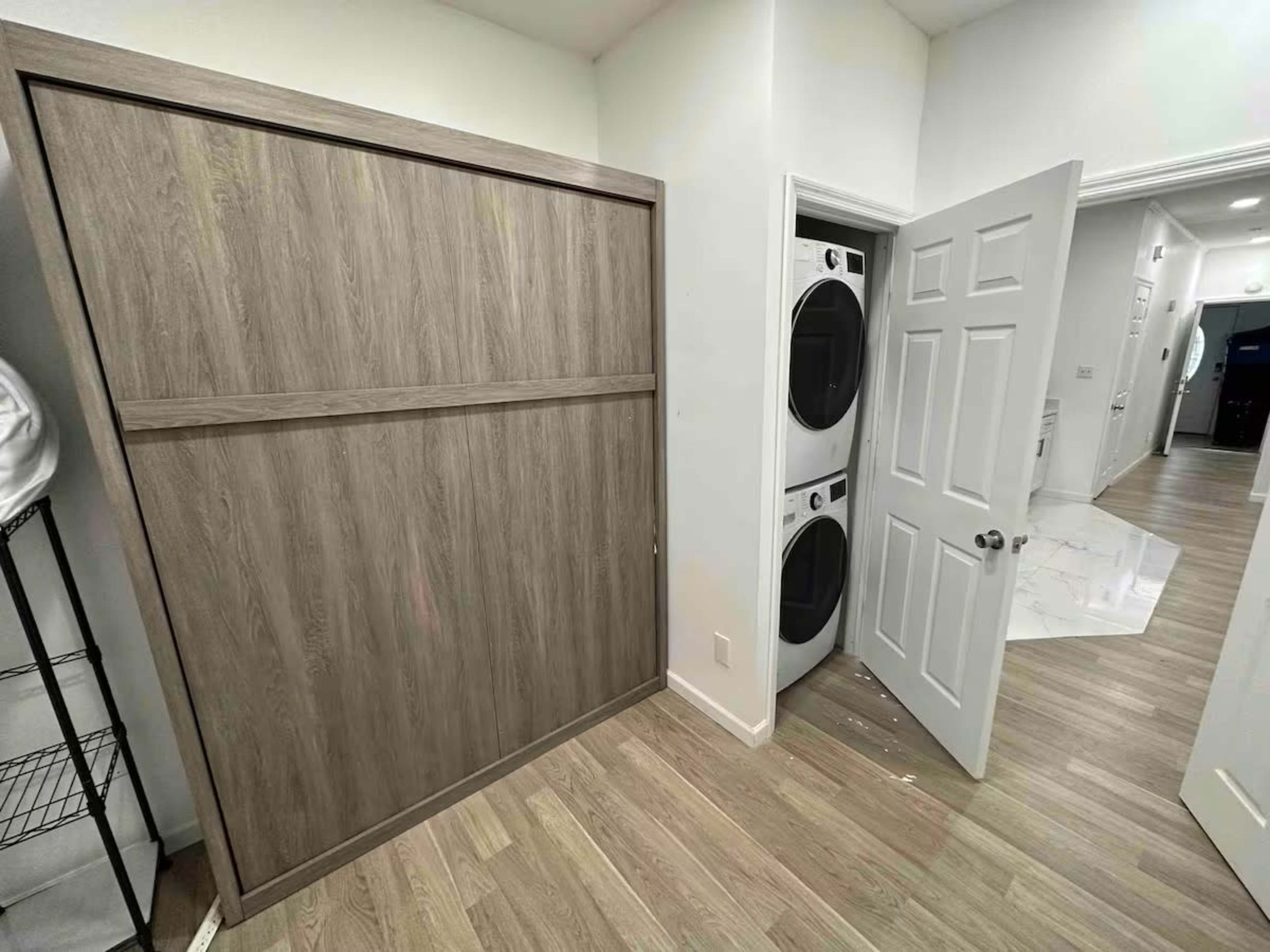 The image shows a laundry area with a stacked washer and dryer next to a wooden foldable wall cabinet.