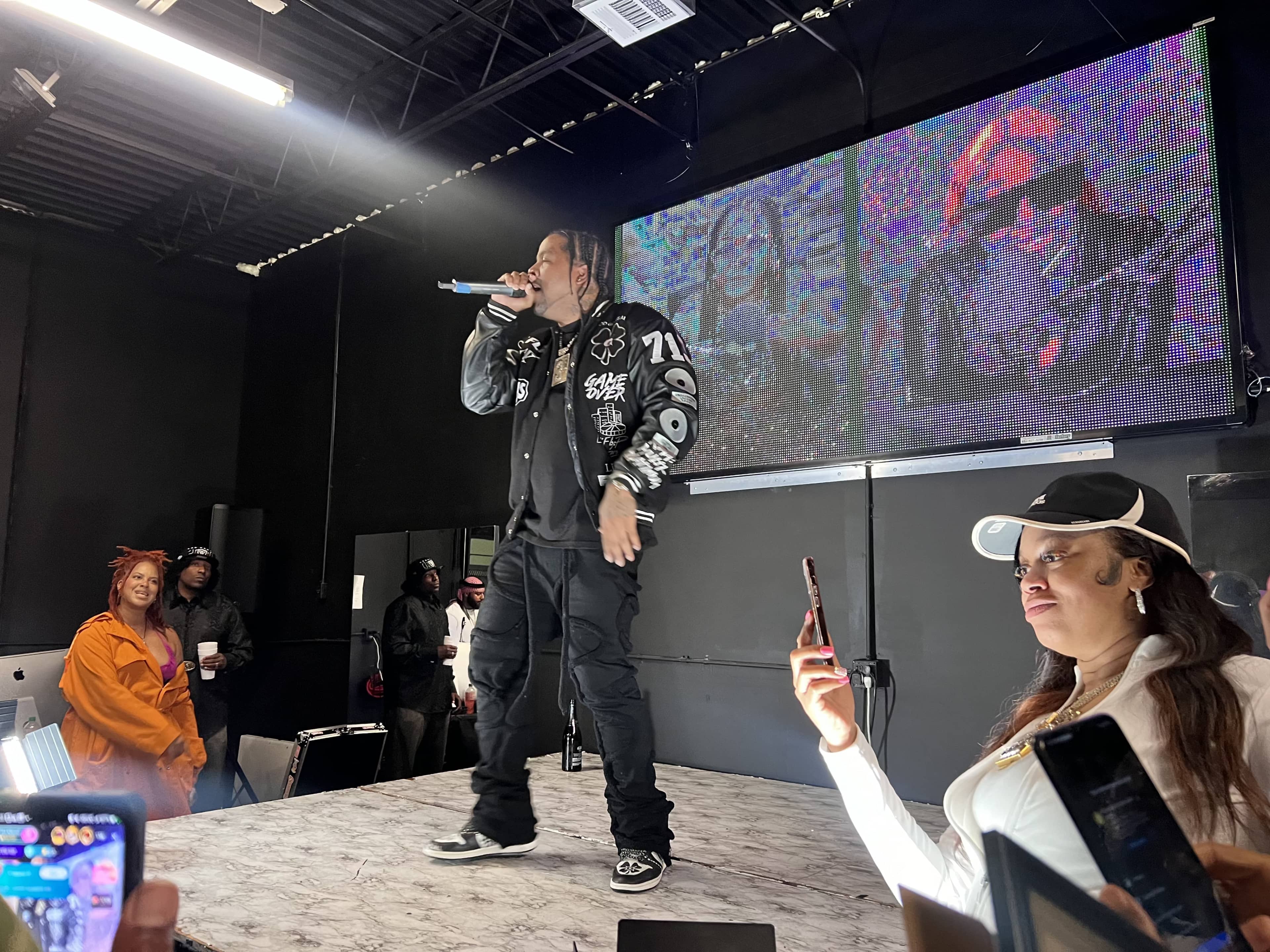 A rapper performs on stage while an audience member records the event on her phone.