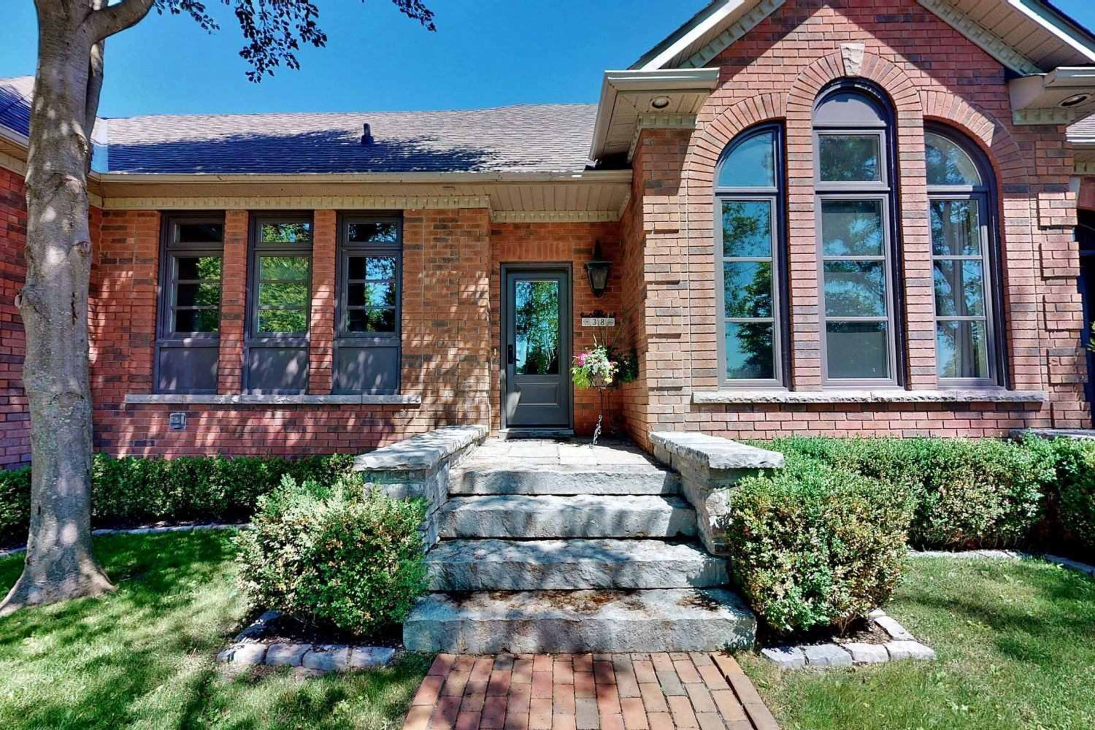 The image shows the exterior of a brick house with large windows, a front door, and a stone walkway leading to the entrance, surrounded by manicured landscaping.
