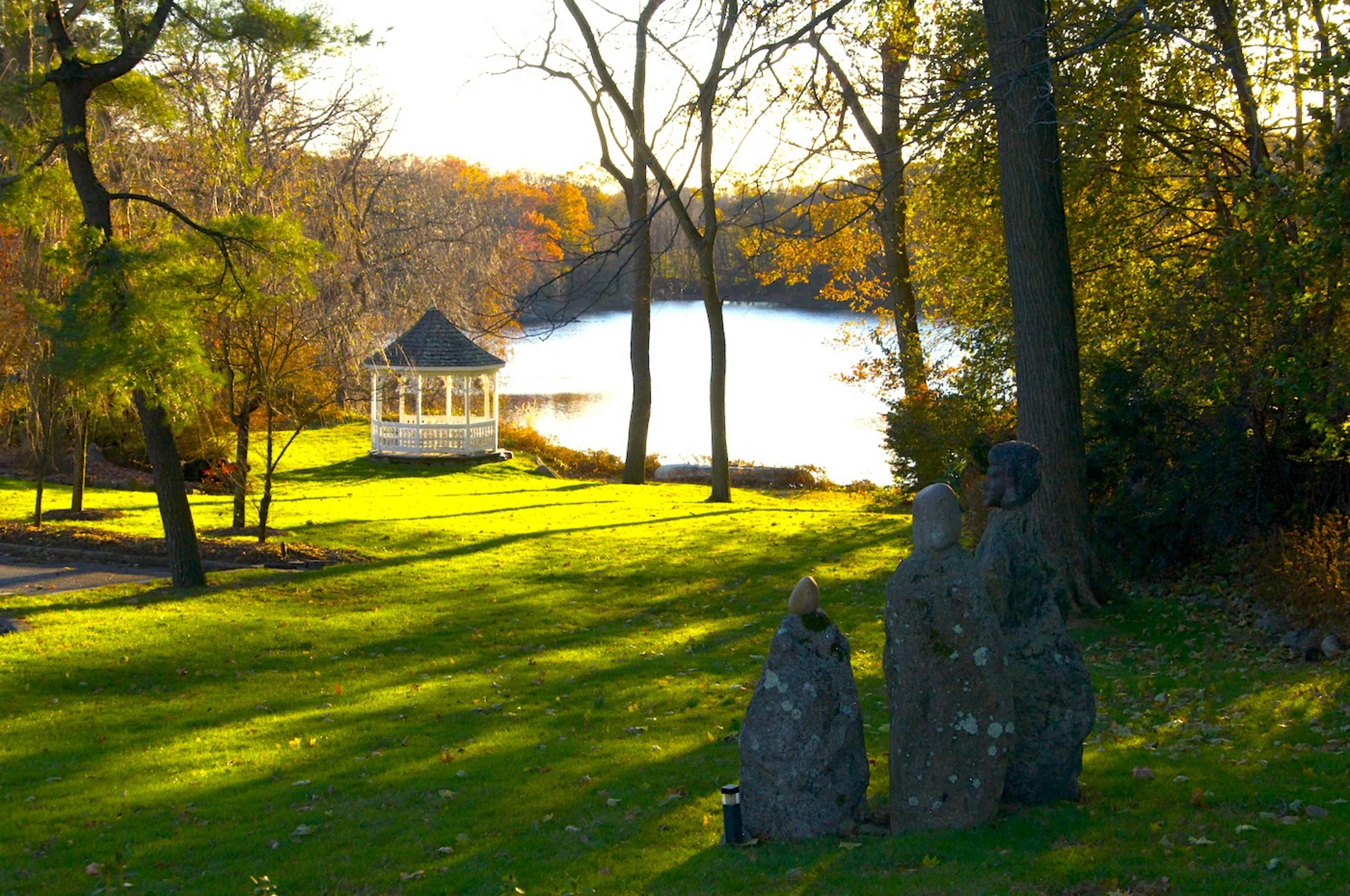 The image shows a serene lakeside scene featuring a gazebo on the water's edge, surrounded by trees and a manicured lawn.