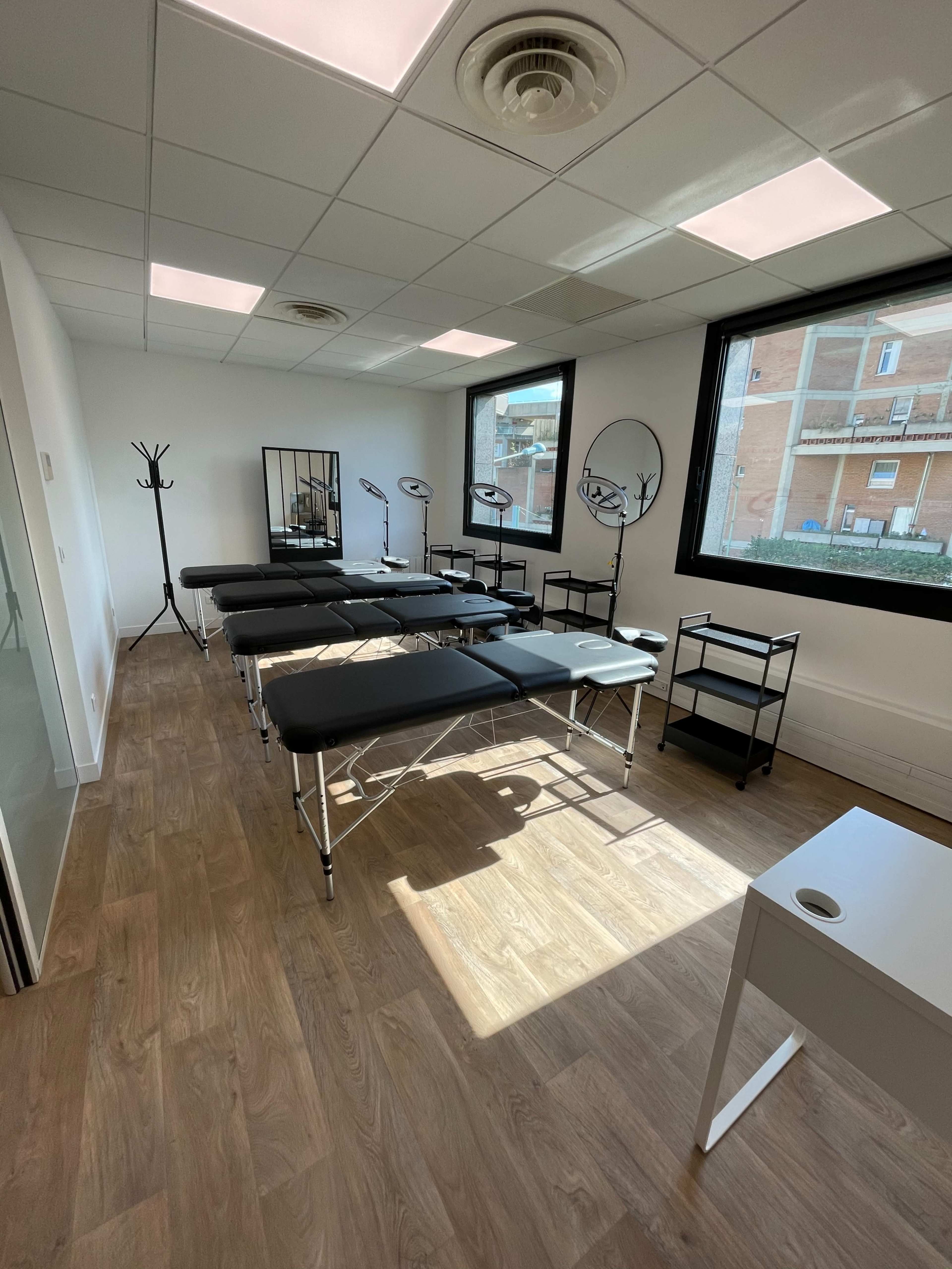 A well-lit room with several massage tables arranged in a line, accompanied by a mirror and mobile carts.