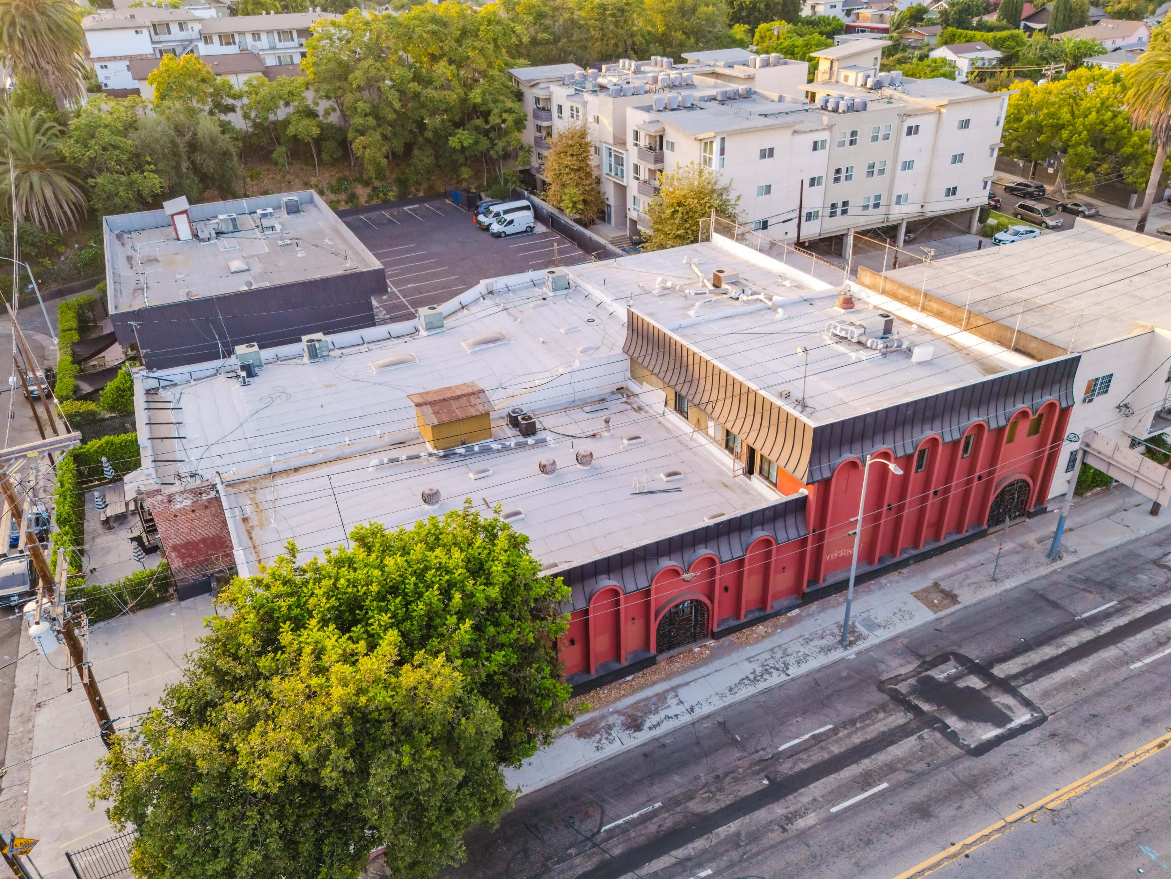 The image shows an aerial view of a building with a red facade and a flat roof, surrounded by trees and parking lots in a residential area.
