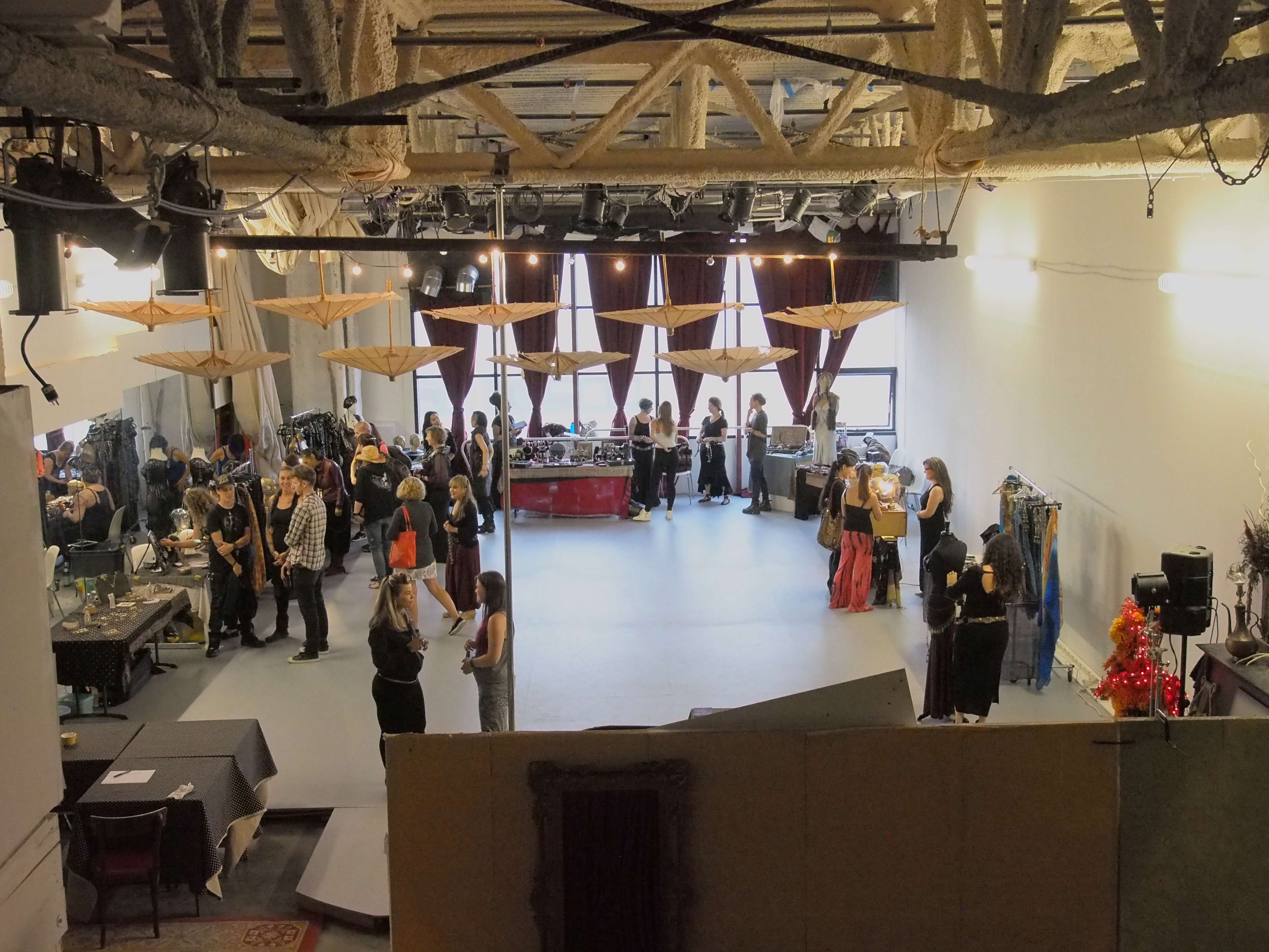 A large studio space is filled with people socializing and preparing for an event, with garments and props arranged on tables around the room.
