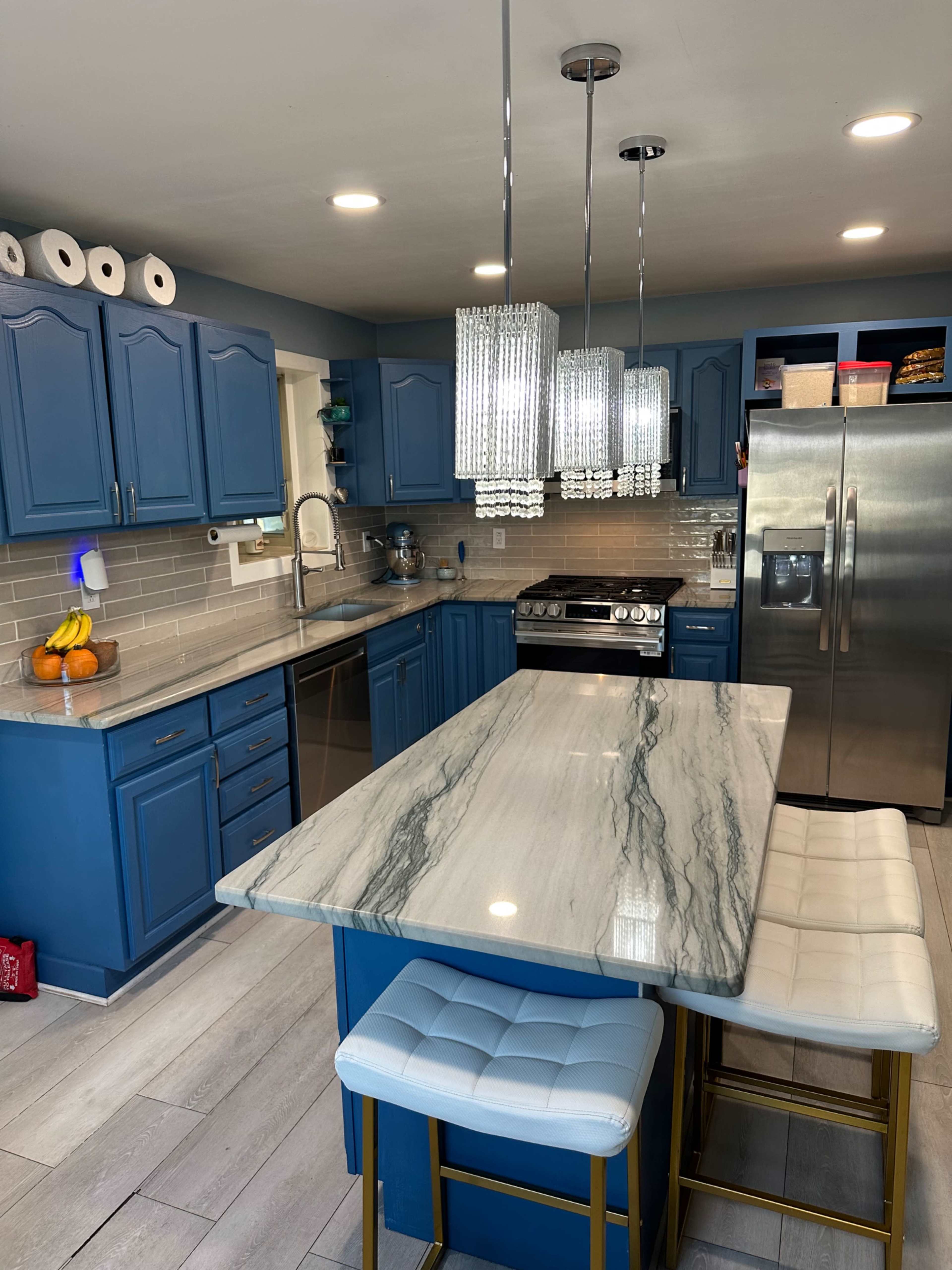 The kitchen features blue cabinets, a marble countertop island with bar stools, and modern pendant lighting above.