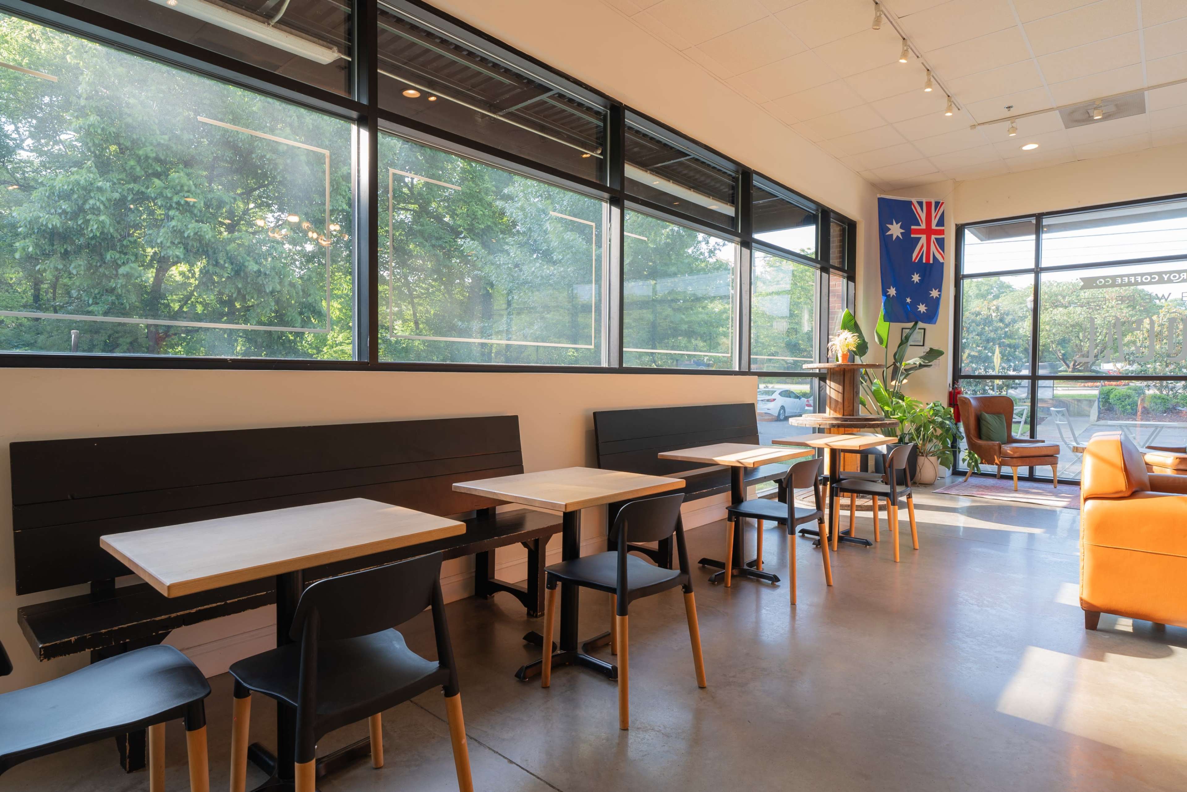 The image shows a coffee shop interior with several wooden tables and chairs, large windows allowing natural light, and an Australian flag hanging on the wall.