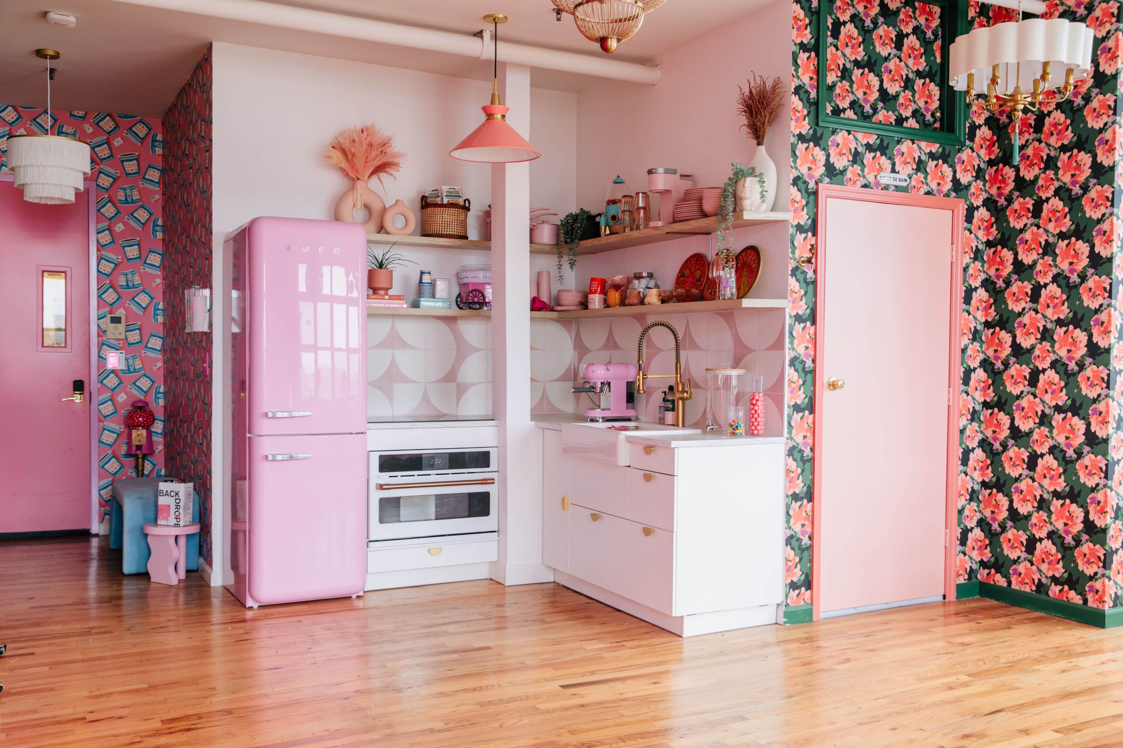 A modern kitchen featuring pink appliances, white cabinetry, and floral wallpaper.
