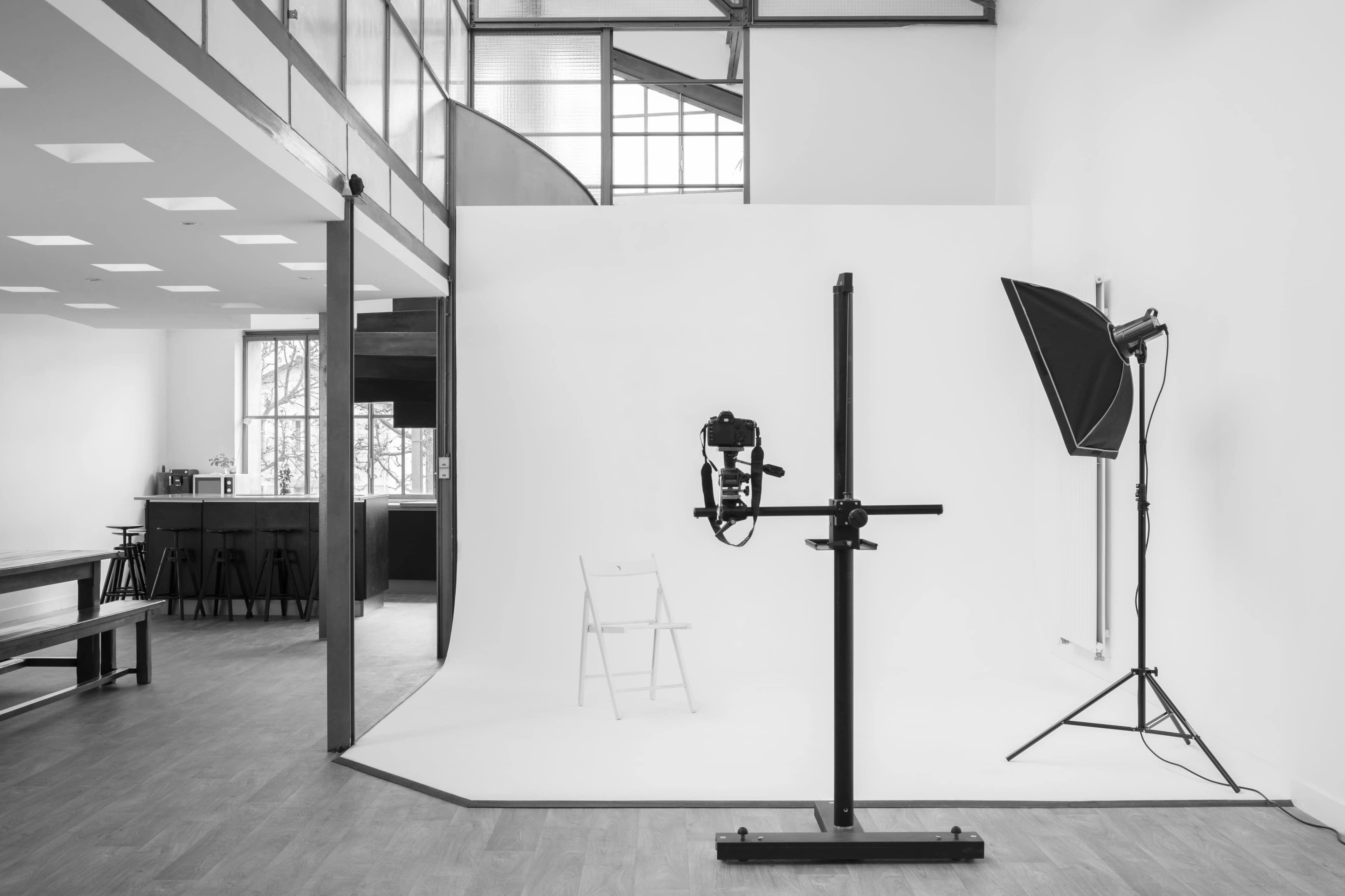 A photography studio with a white backdrop, a chair, and lighting equipment set up in a spacious room with modern architectural features.