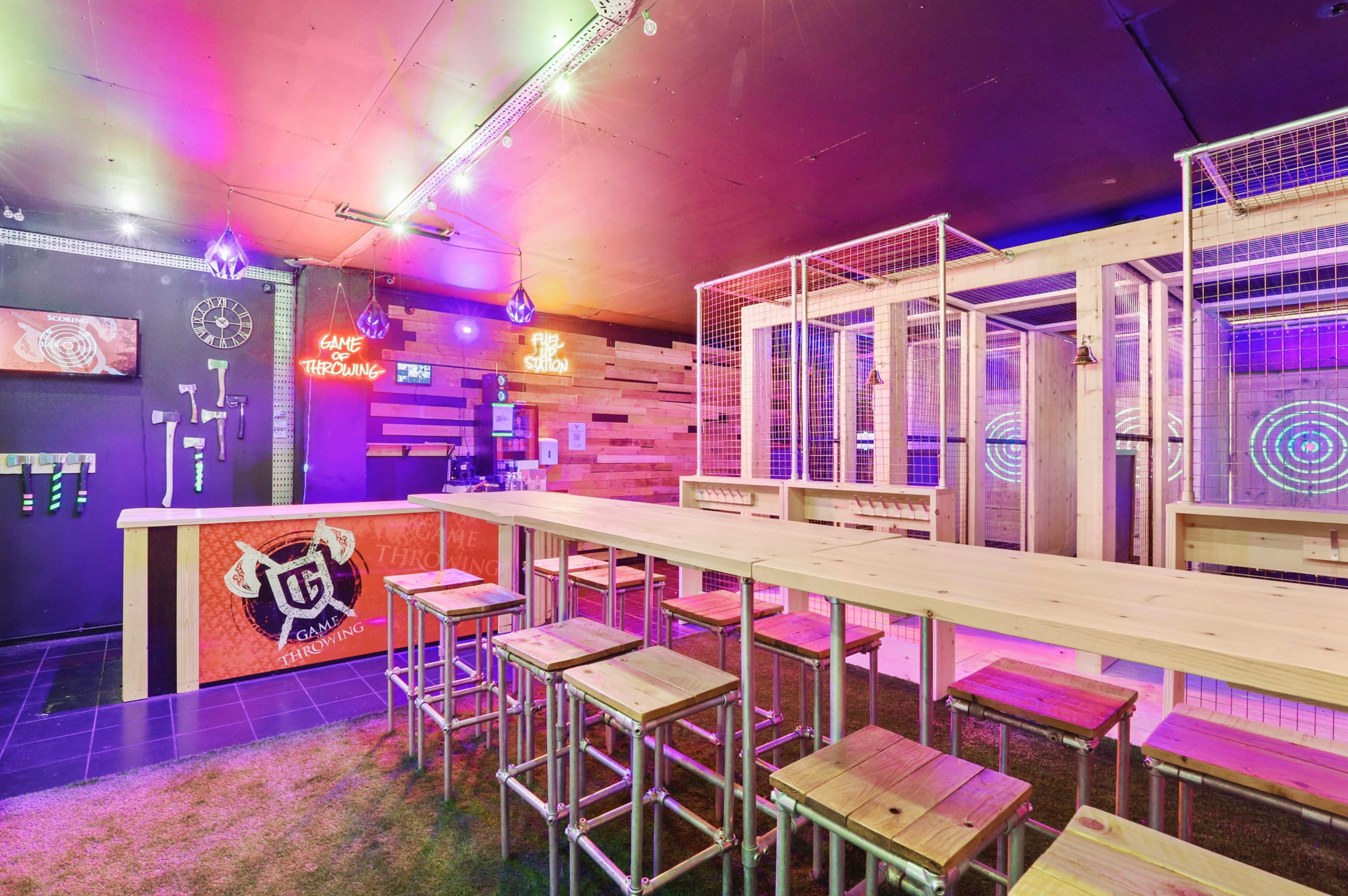A modern gaming lounge with a wooden bar, stools, and illuminated targets on the walls.