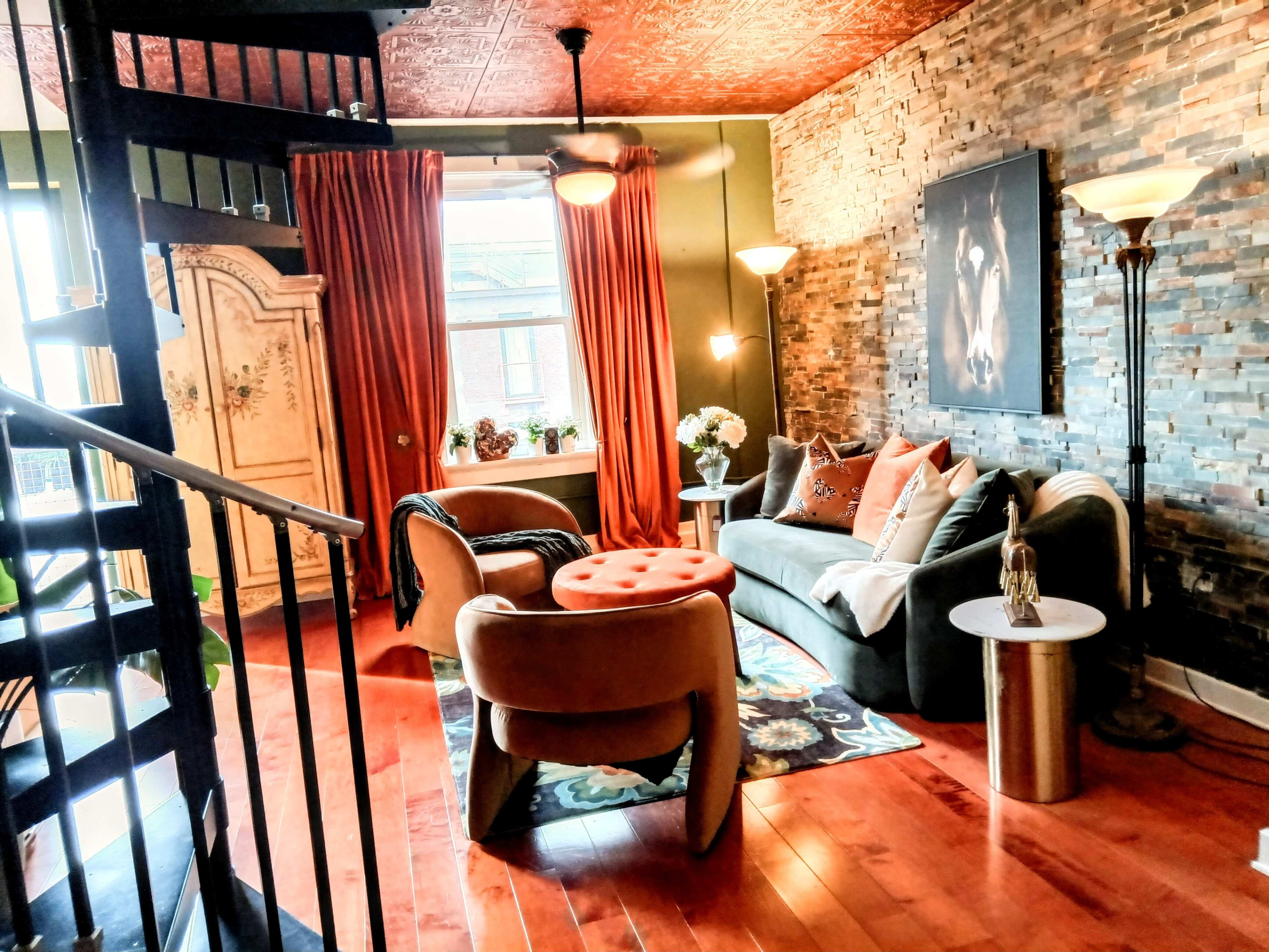 A cozy living room with a spiral staircase, stone-accented walls, large windows, and stylish furniture, including a sofa and a round coffee table.