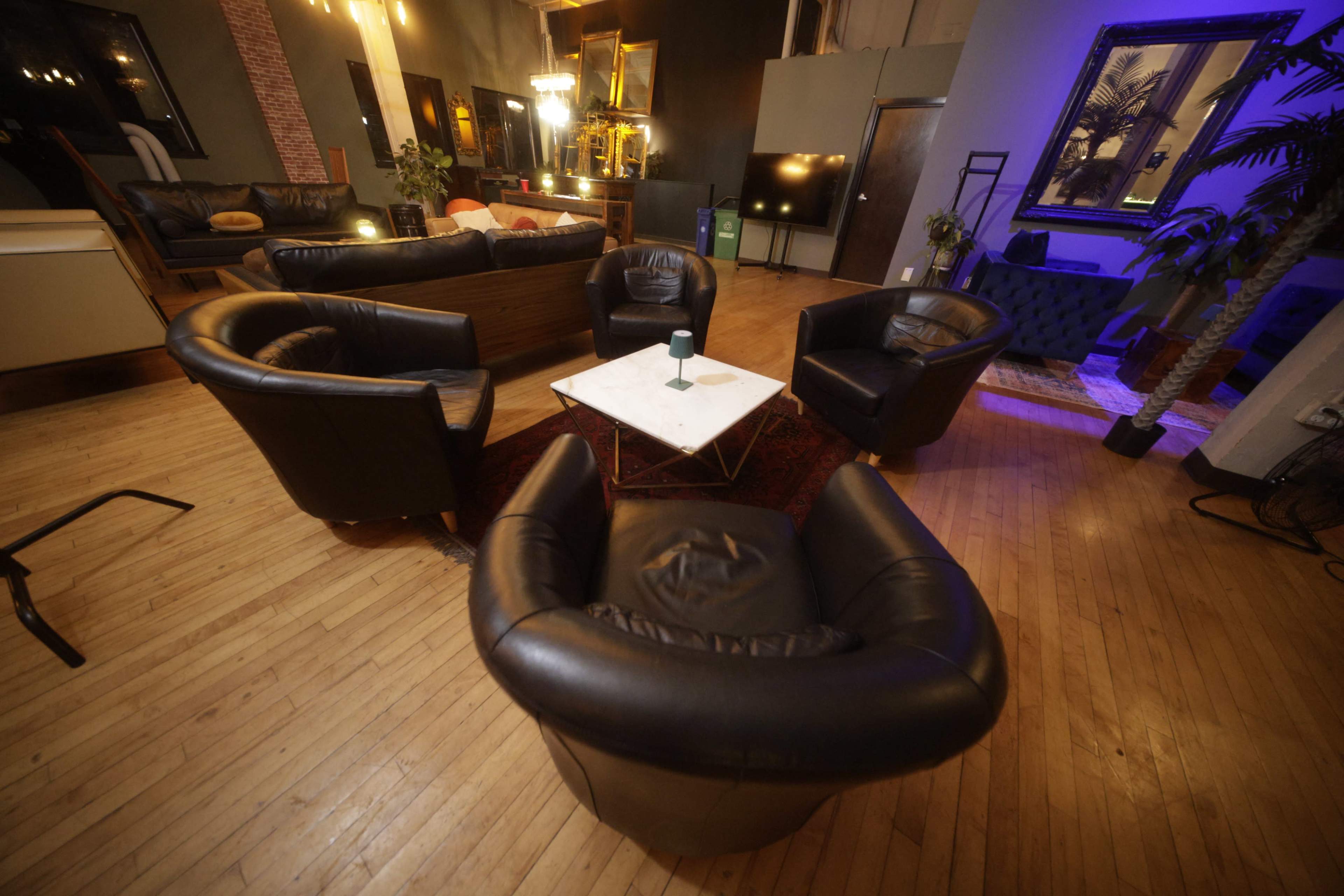 The image shows a cozy lounge area with four black leather chairs arranged around a marble-top coffee table on a wooden floor.