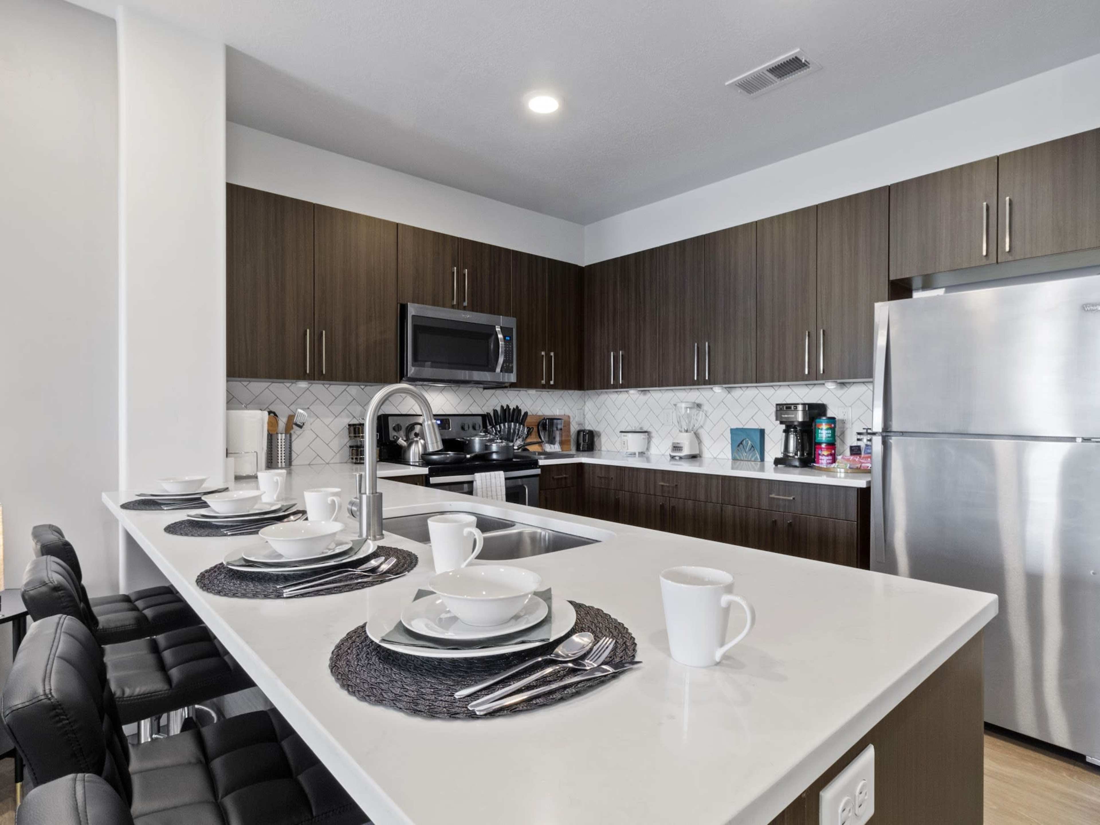 A modern kitchen features dark wooden cabinets, a stainless steel refrigerator, and a countertop set with dishes and utensils.