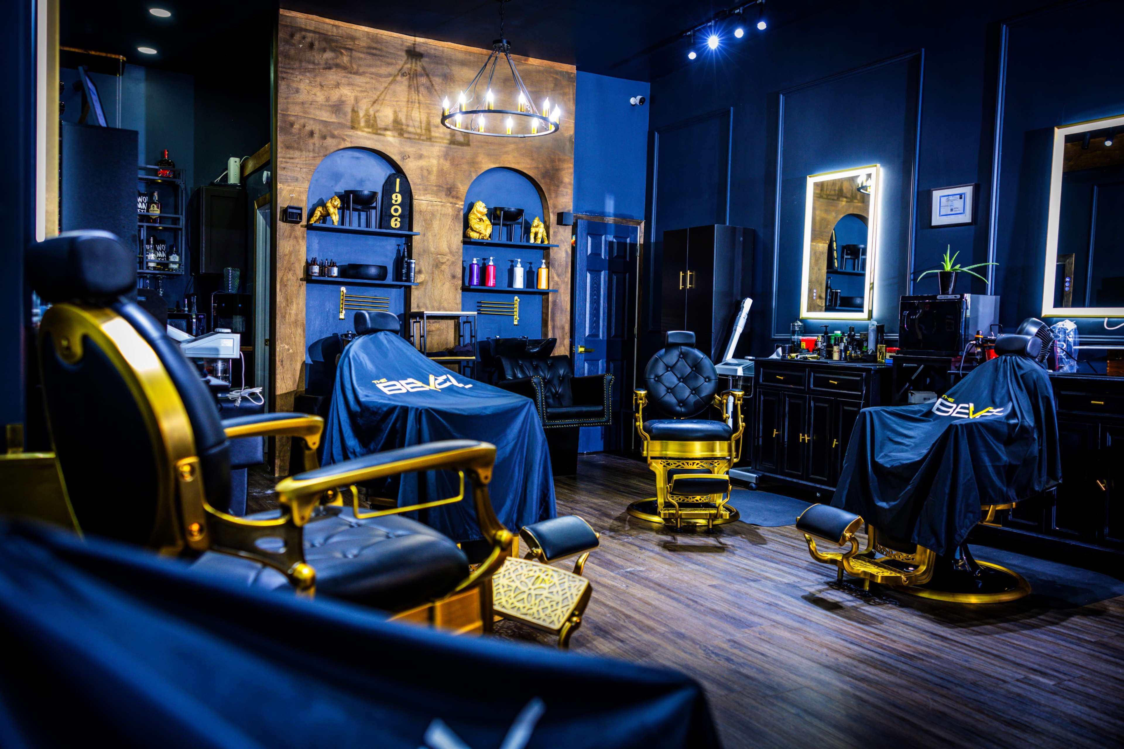 The image shows a modern barbershop interior featuring gold-accented barber chairs, wooden decor, and illuminated mirrors.