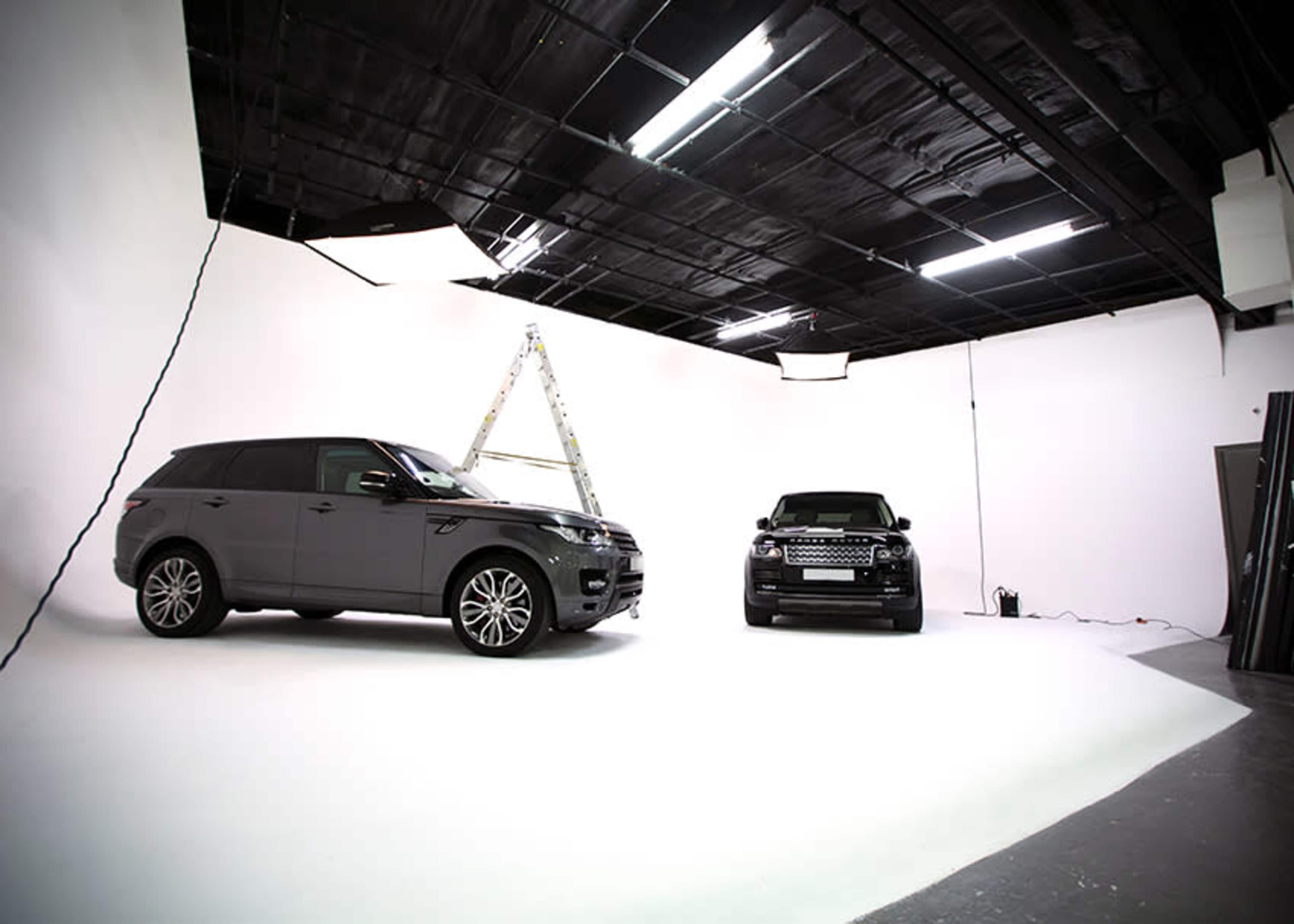 Two luxury SUVs parked in a photography studio with a ladder set up in the background.