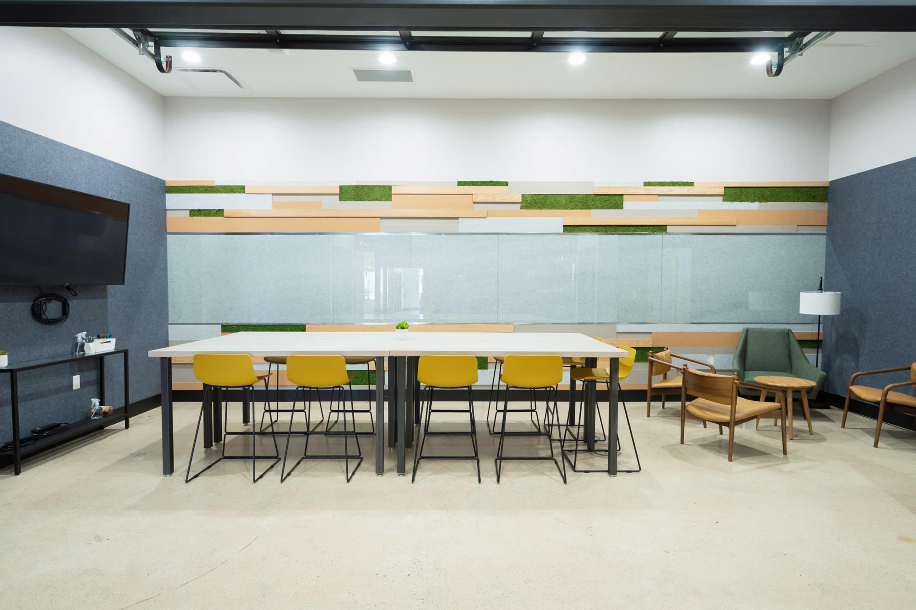 The image shows a modern meeting room with a large table surrounded by yellow chairs, a glass wall, and decorative wooden panels.