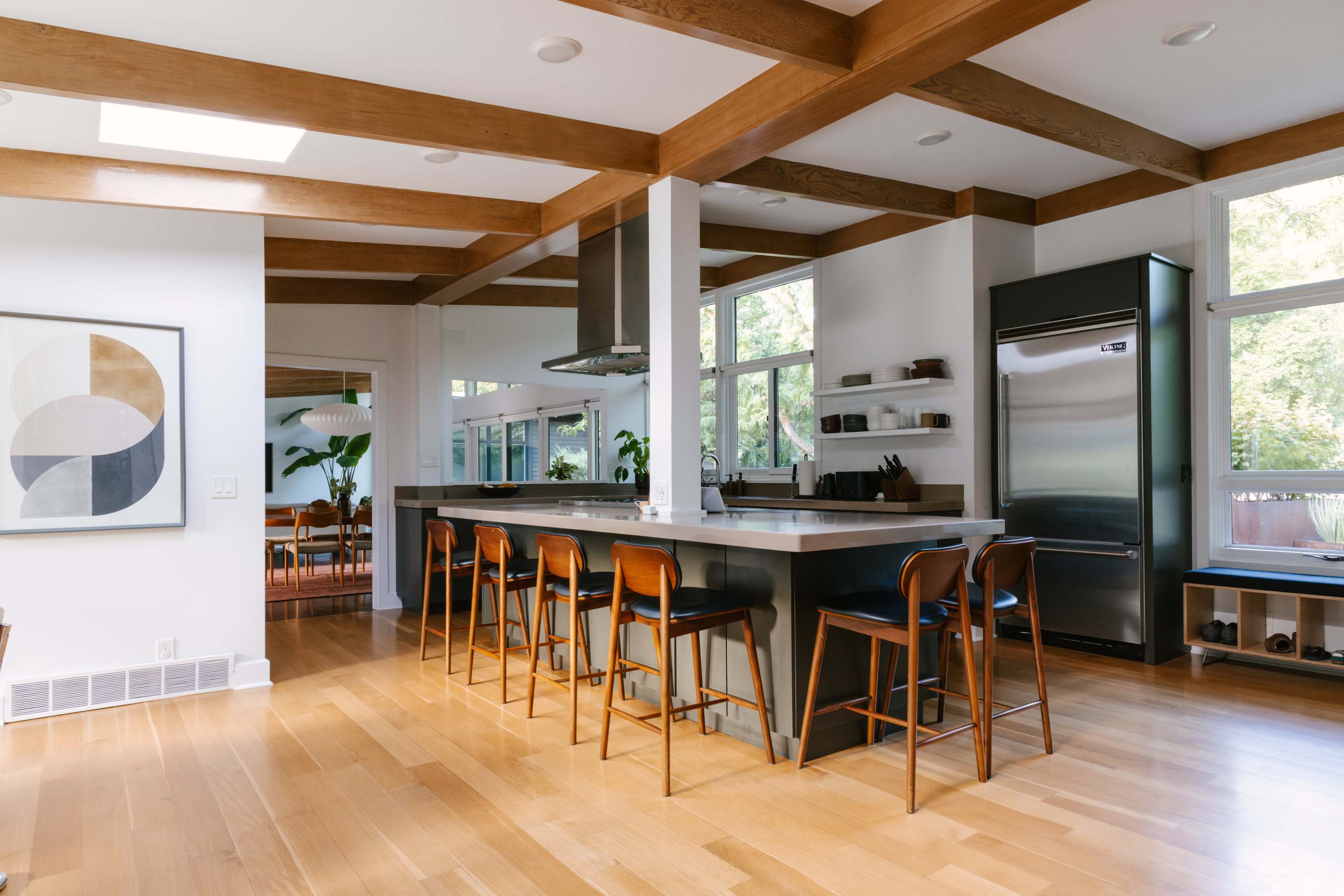 The image shows a modern kitchen with a large island, wooden beams on the ceiling, and bar stools arranged around the island.