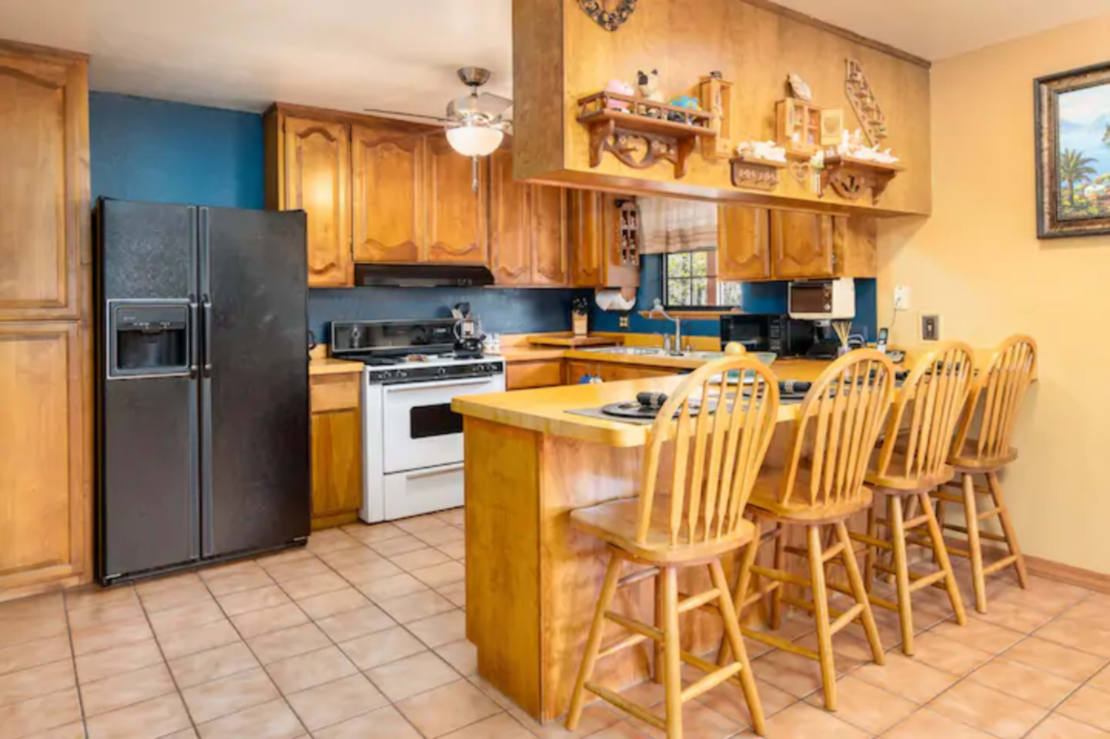 The kitchen features wooden cabinets, a large island with seating for four, and appliances including a black refrigerator and a white gas stove.