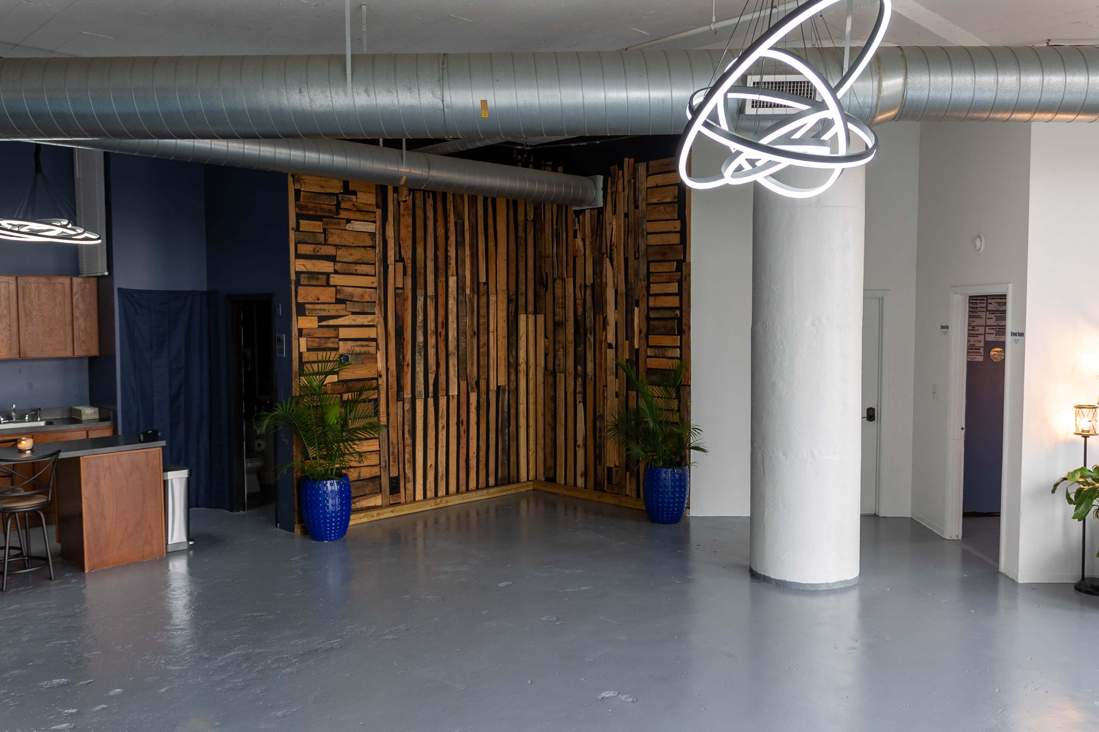 A spacious interior with a wooden wall, a kitchen area, and large light fixtures.