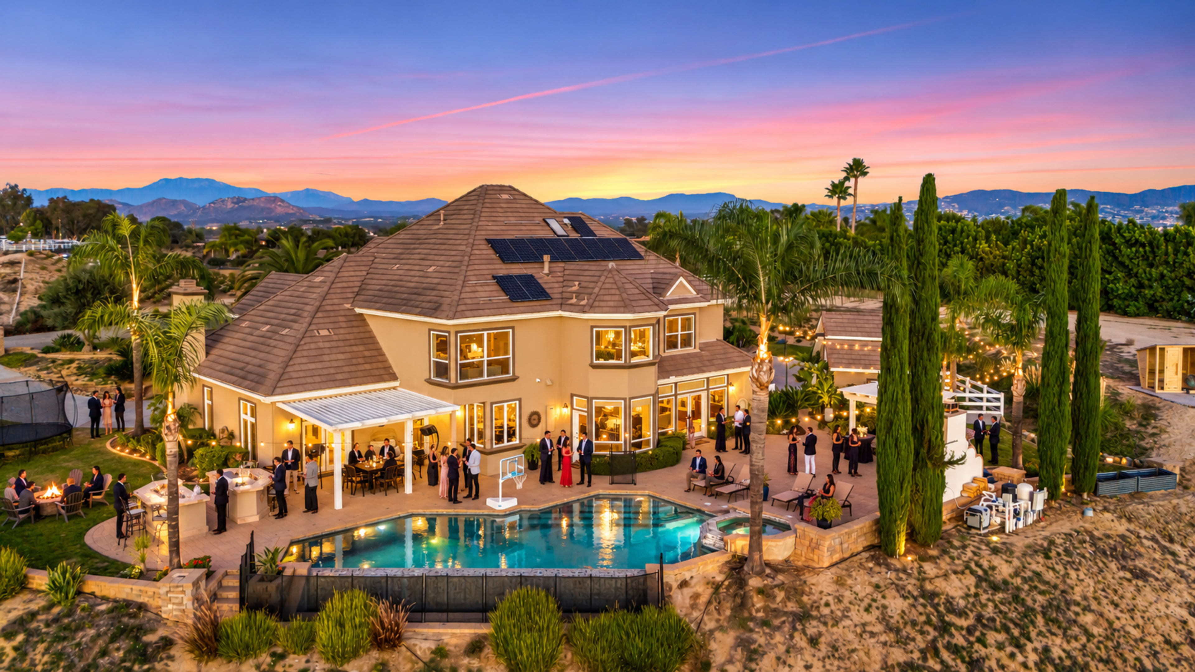 A large, well-lit house with a pool sits in a landscaped yard, surrounded by guests enjoying an outdoor gathering at sunset.