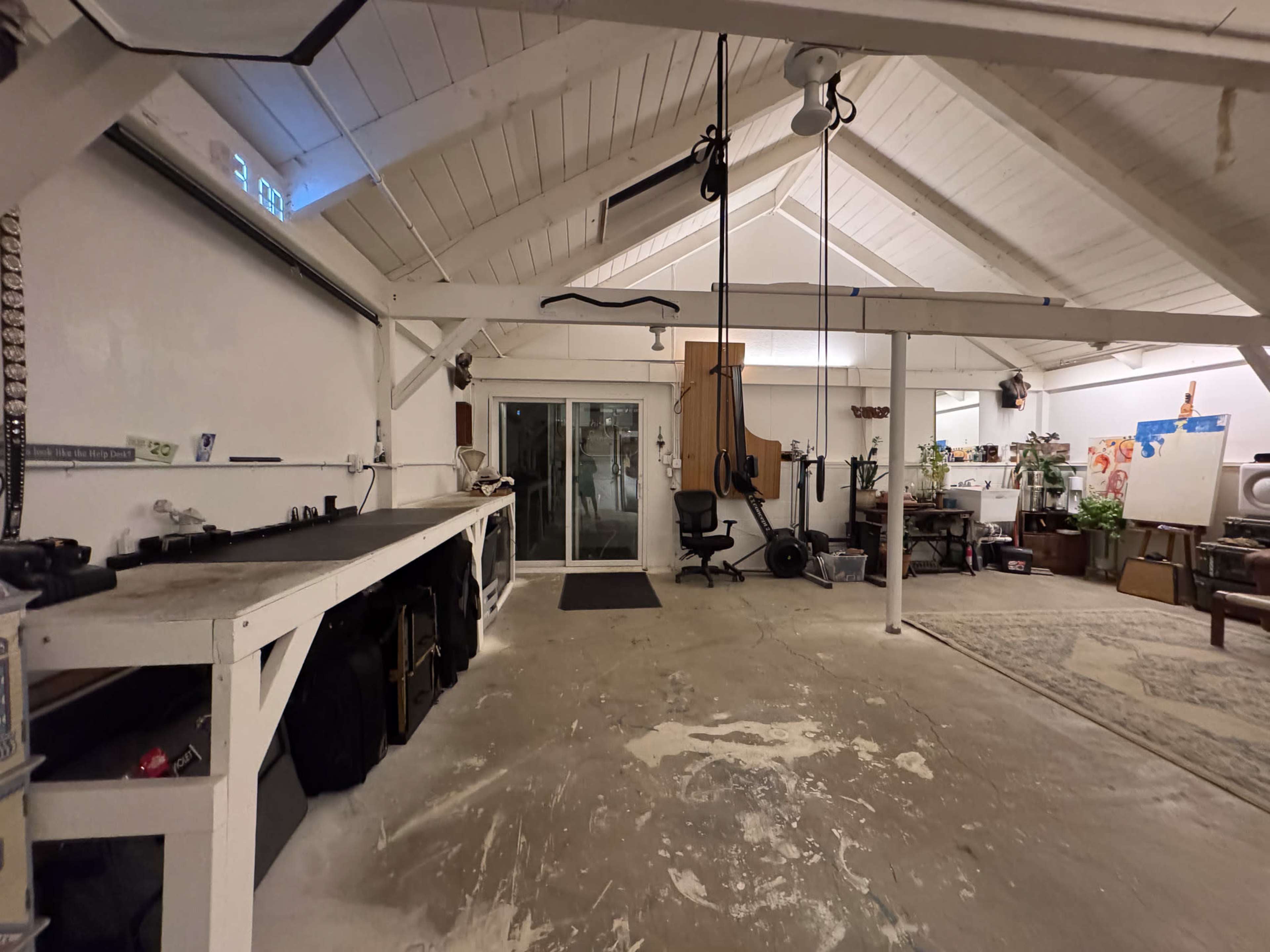 The image shows a spacious workshop with a high, white ceiling, including a workbench on the left and various equipment scattered around.