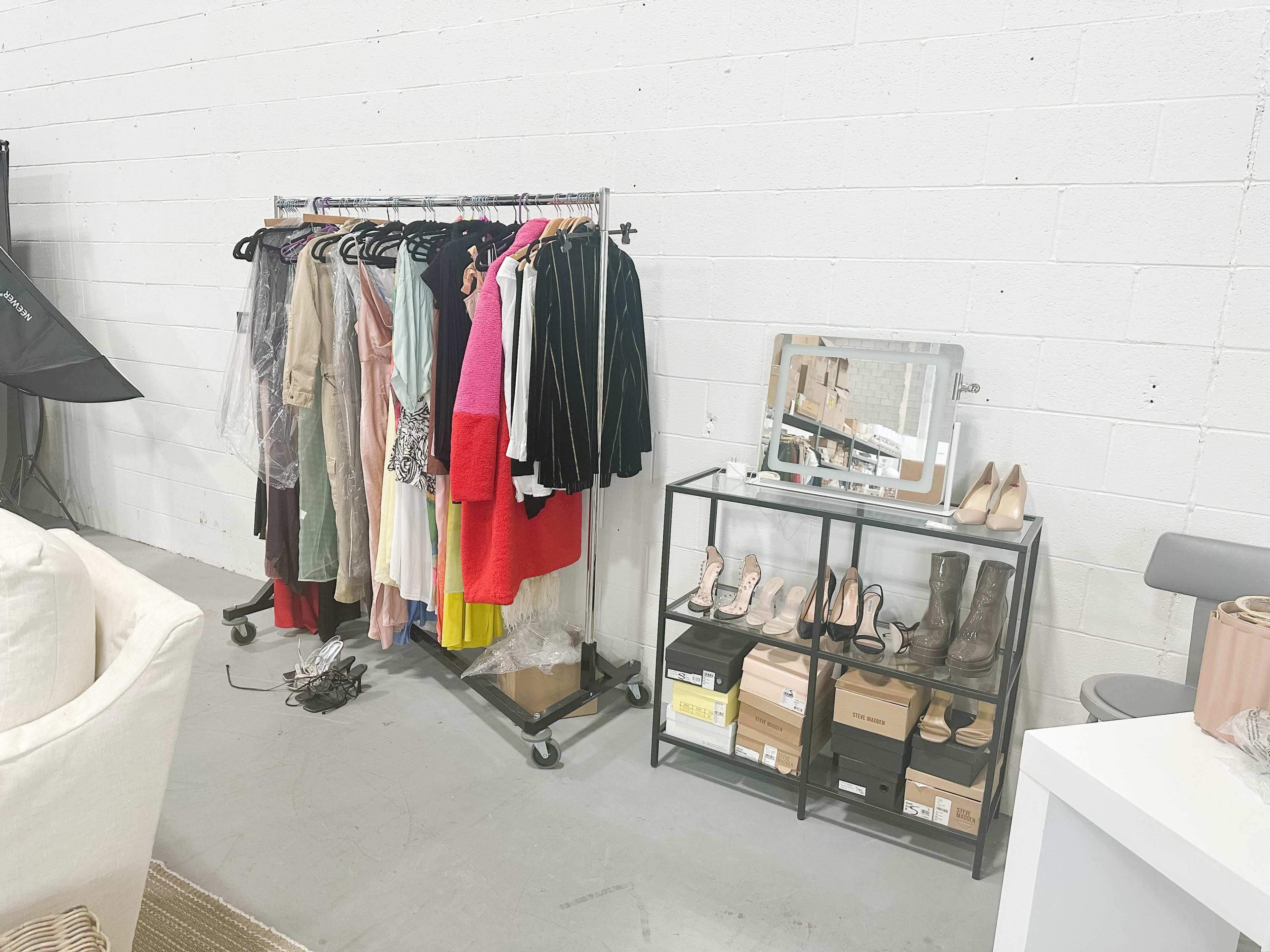 A clothing rack with various garments hangs beside a display stand holding shoes and boxes in a studio setting.