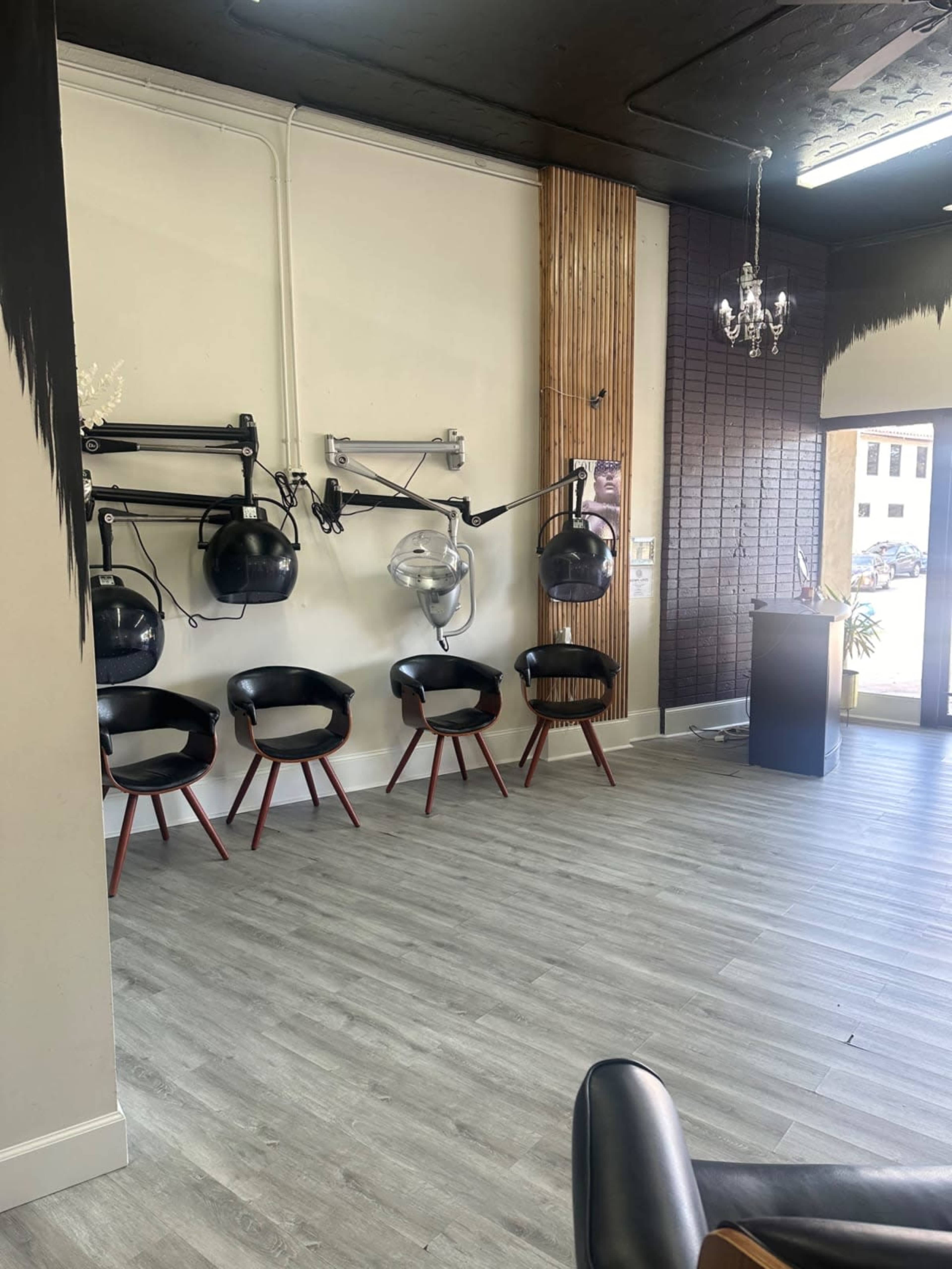 The image shows a salon interior featuring black chairs arranged in front of wall-mounted hair dryers and a reception area with a doorway.