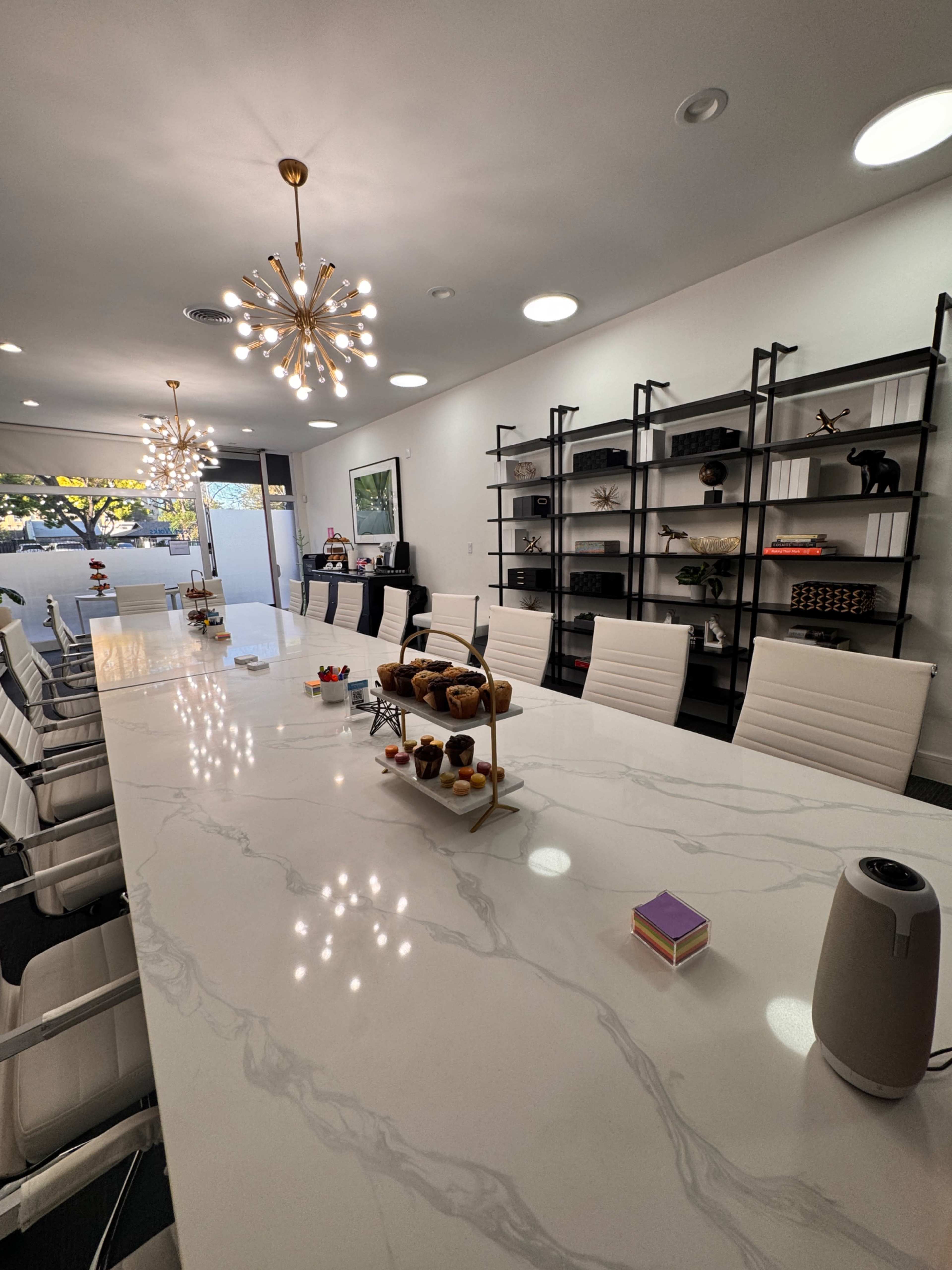 The image shows a modern conference room with a long marble table, white leather chairs, and shelves displaying various decorative items.