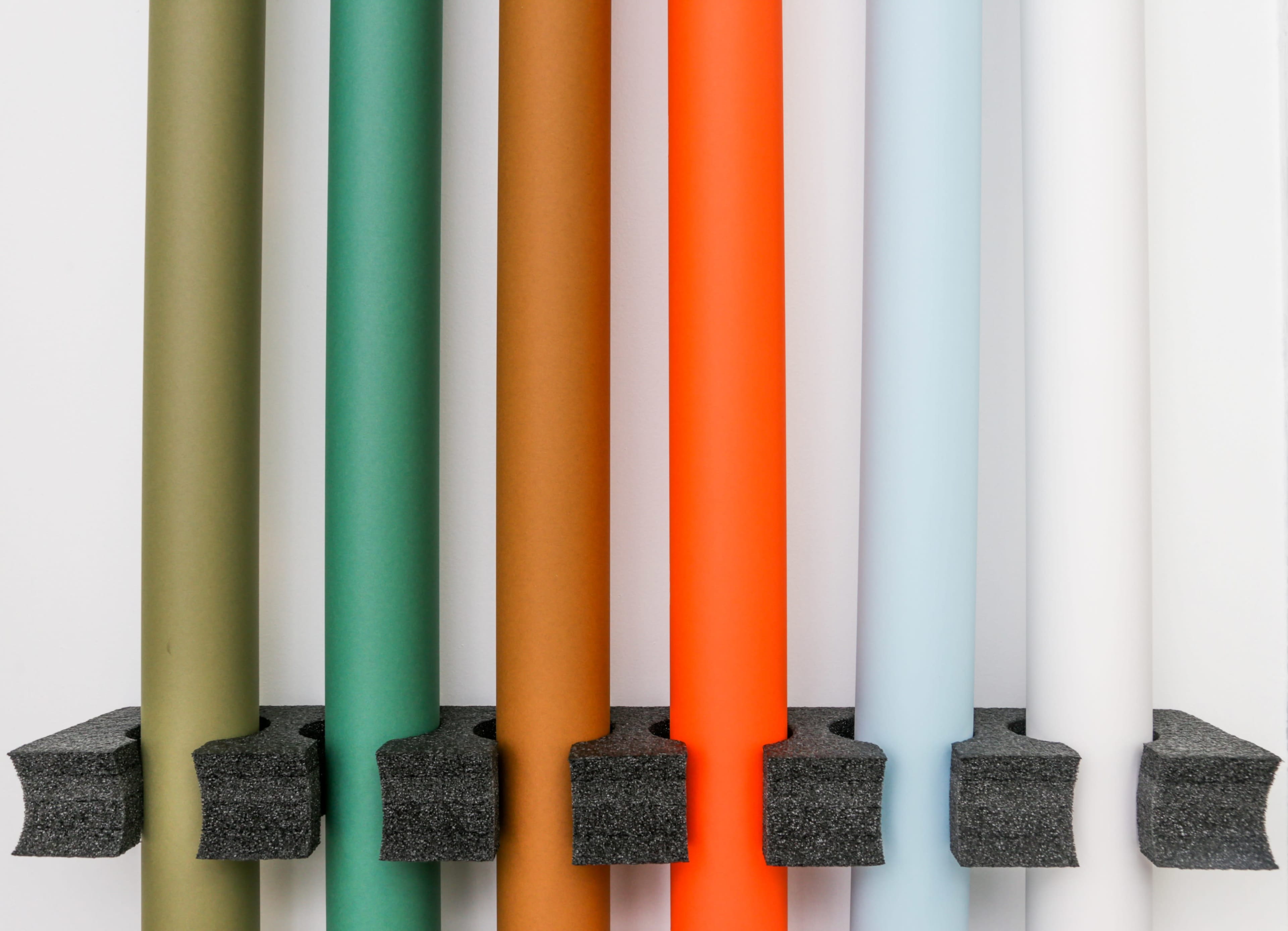 A series of vertically arranged colored paper rolls are mounted on a black holder against a white background.