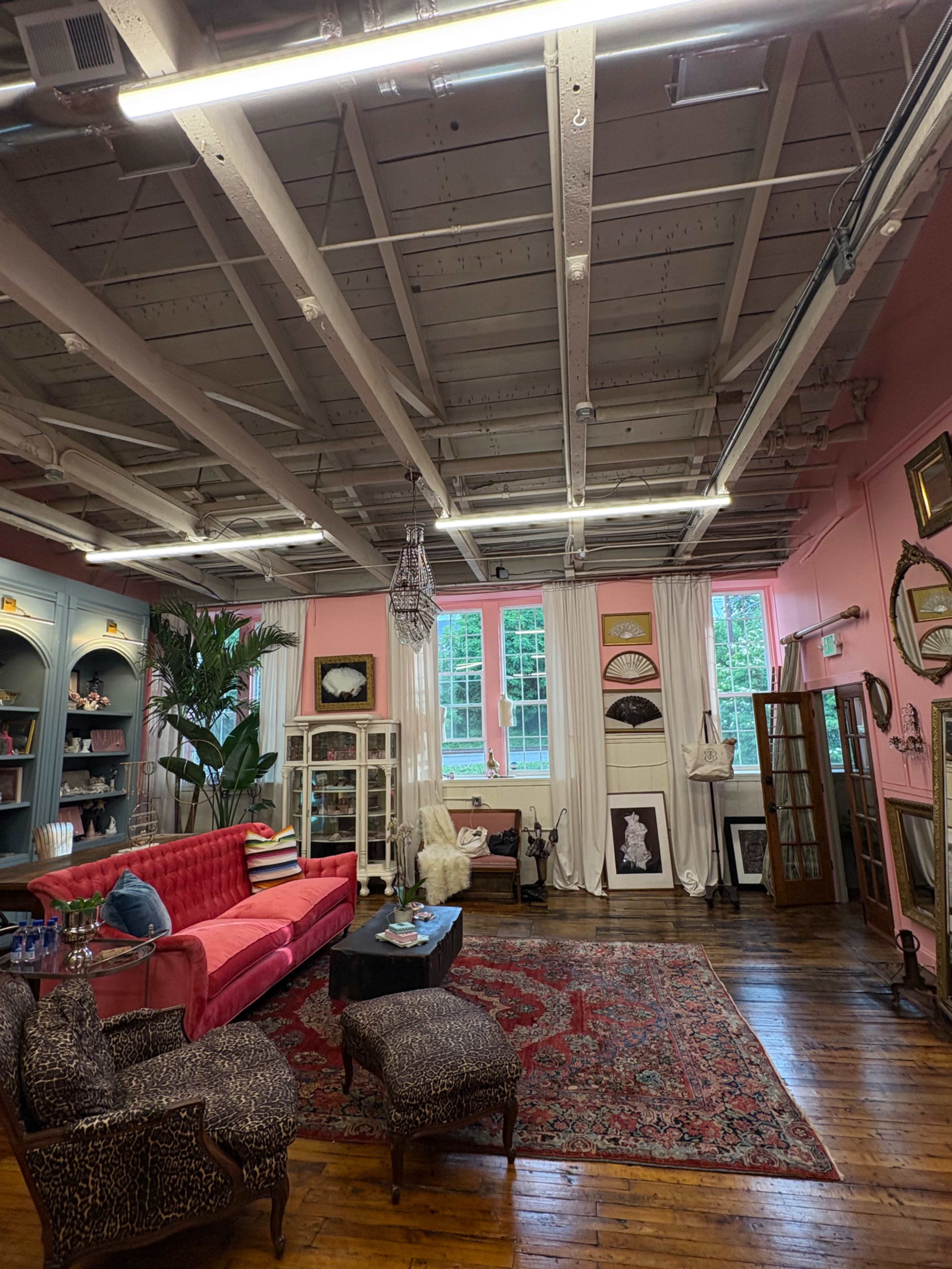 The image shows a bright, stylish interior of a room featuring pink walls, vintage furniture, a large area rug, and decorative frames on the walls.