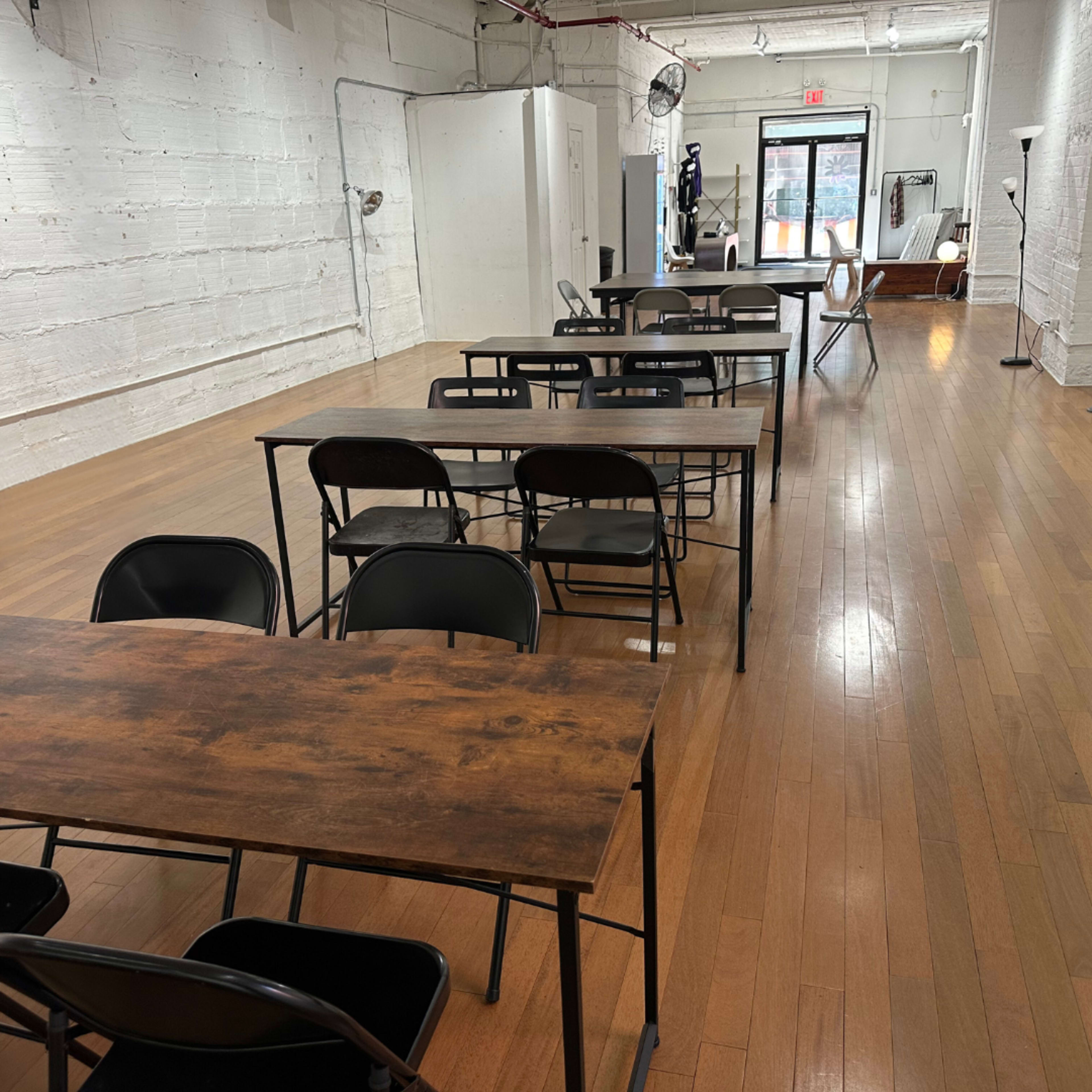 An empty room with several metal folding tables and chairs arranged in rows on a wooden floor.