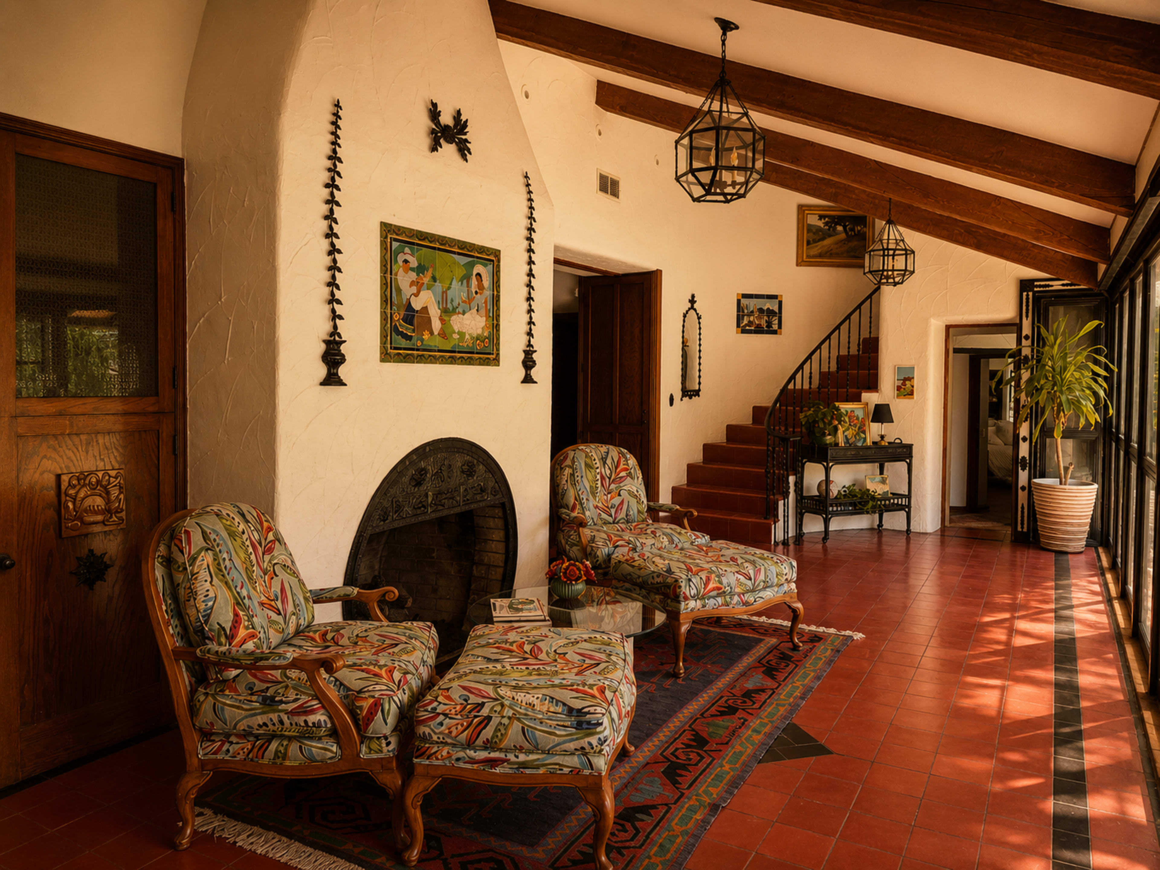 The image depicts a spacious indoor area with two patterned chairs, a fireplace, and a staircase leading to an upper level, framed by large windows.