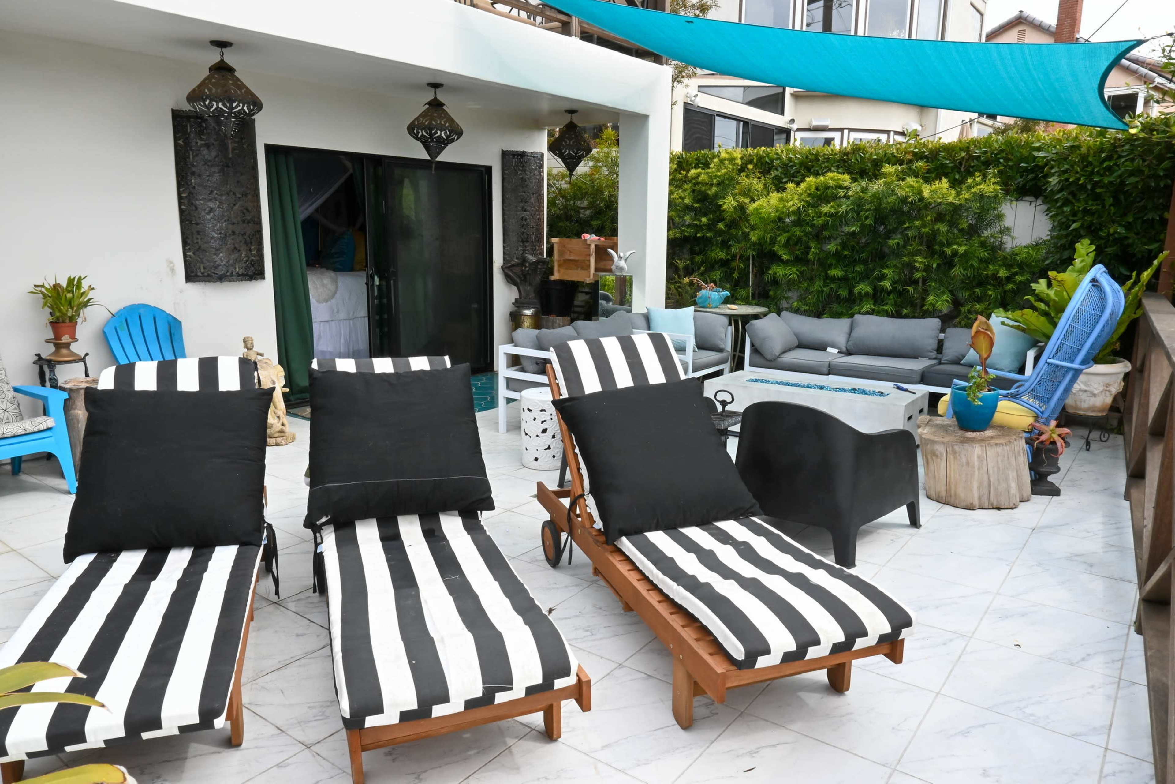 A patio area with striped lounge chairs, a gray outdoor sofa, and decorative plants, all under a shaded canopy.