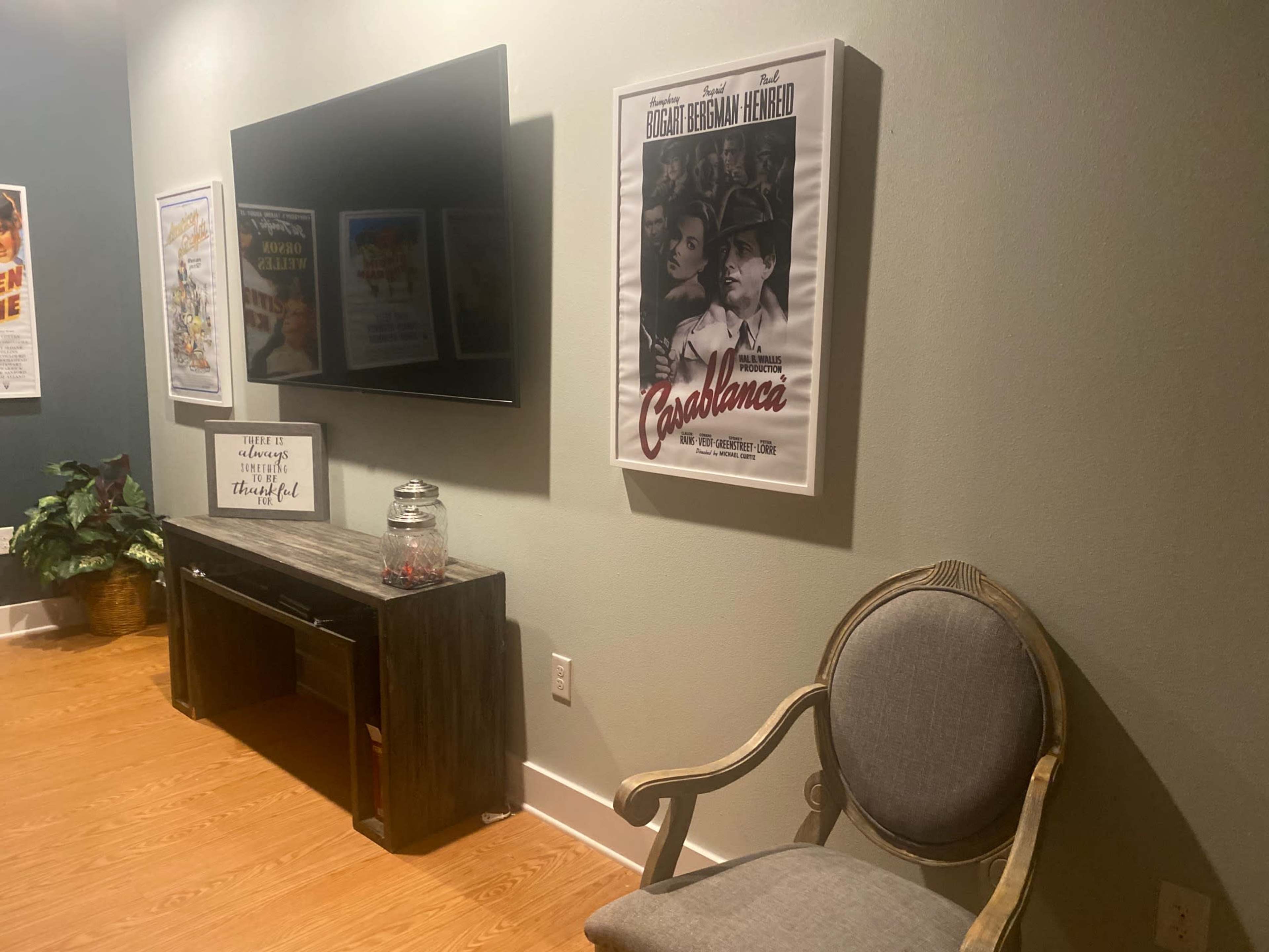A cozy room features a television mounted on the wall, a vintage movie poster of "Casablanca," and a wooden console table beside a decorative chair.