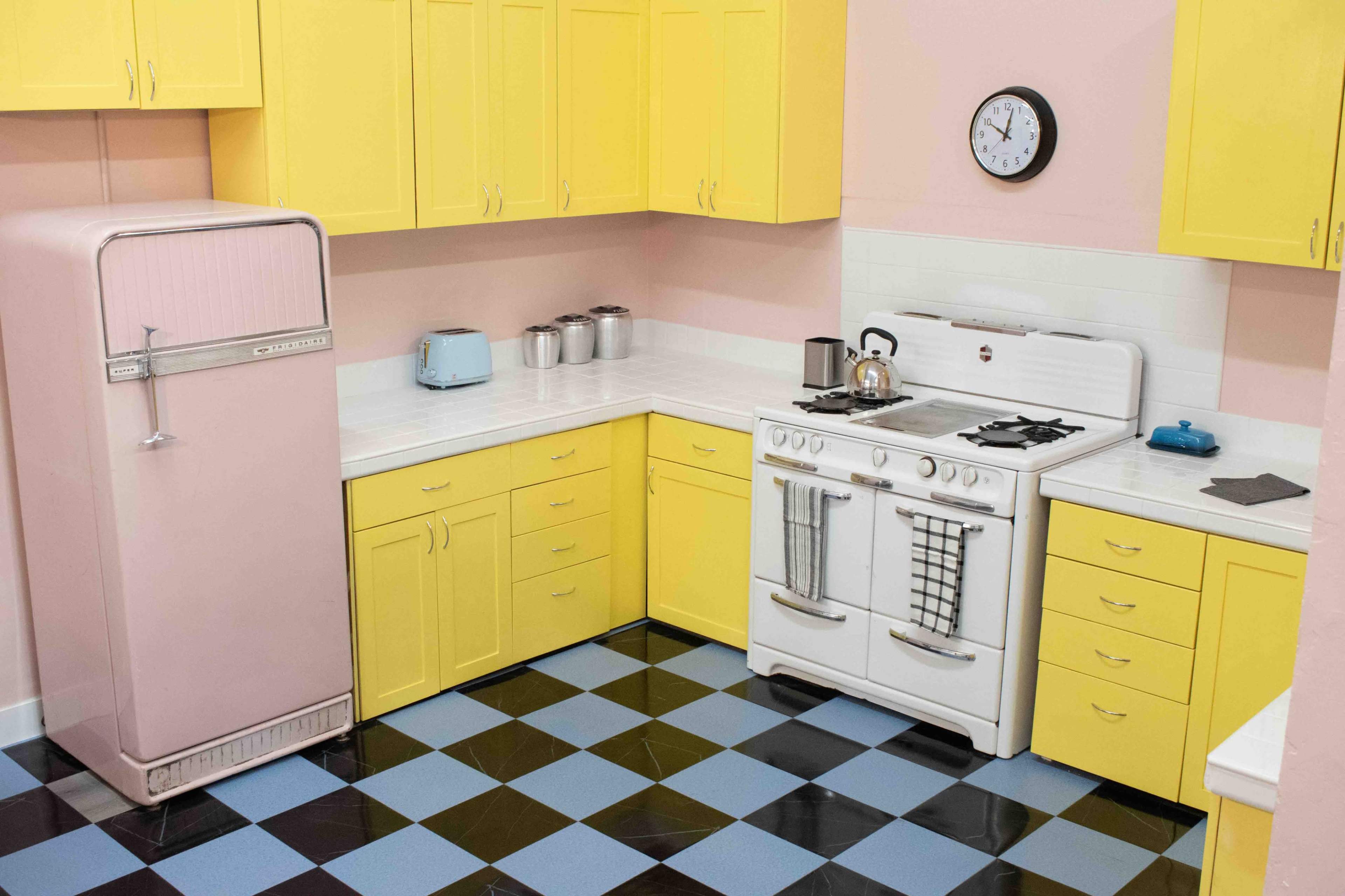 A kitchen with yellow cabinets, a pink refrigerator, and a white stove on a checkered black and blue floor.