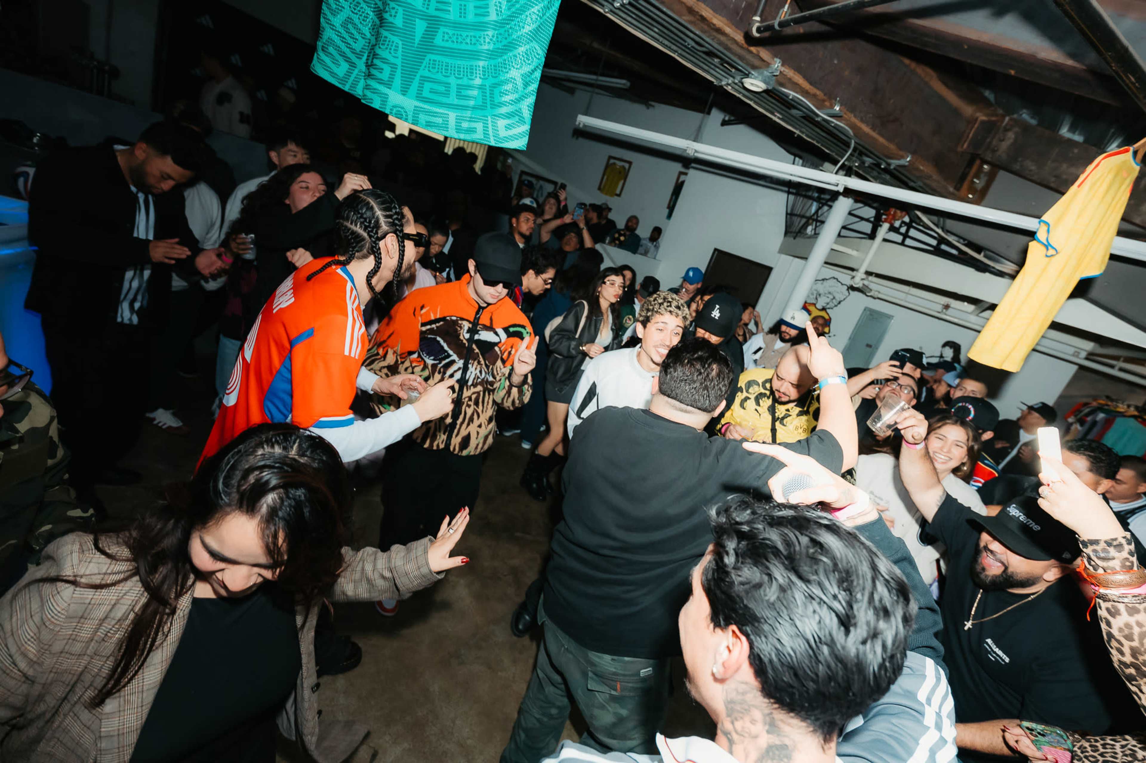 A lively crowd dances and socializes in a dimly lit warehouse space.