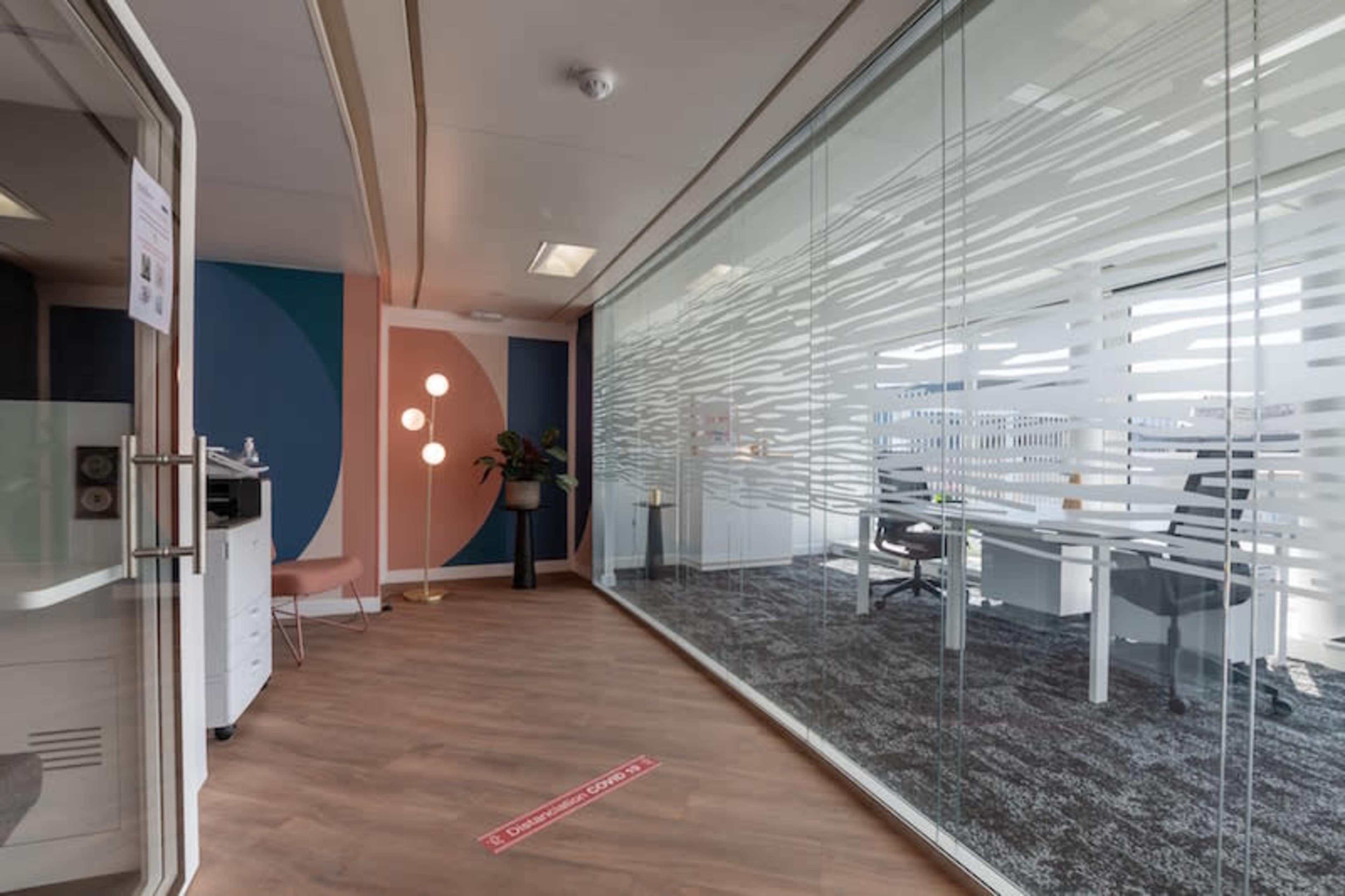 A modern office space with a glass-walled conference area, wooden flooring, and a colorful accent wall.