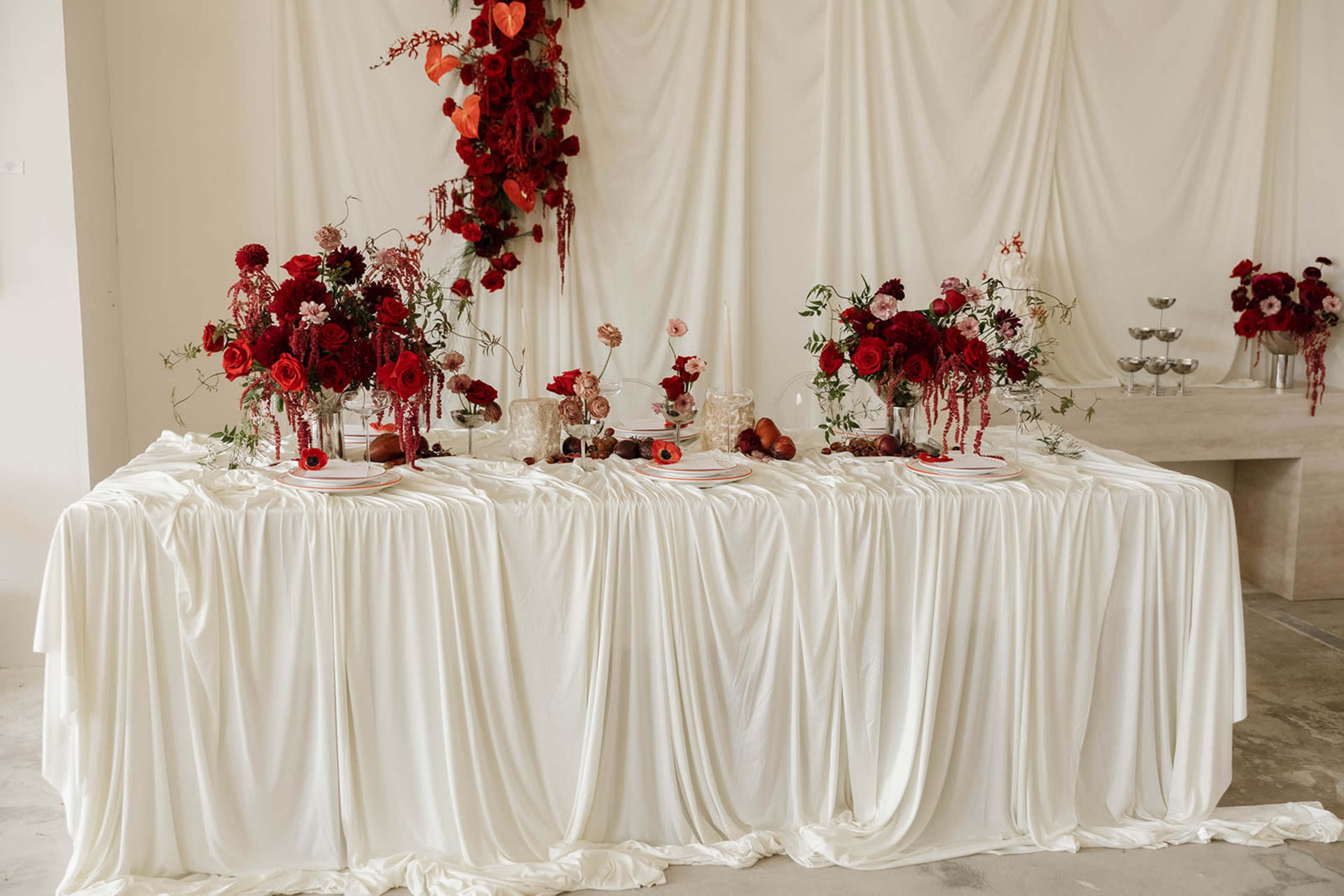 A table adorned with white draping features vibrant red floral arrangements and decorative elements.