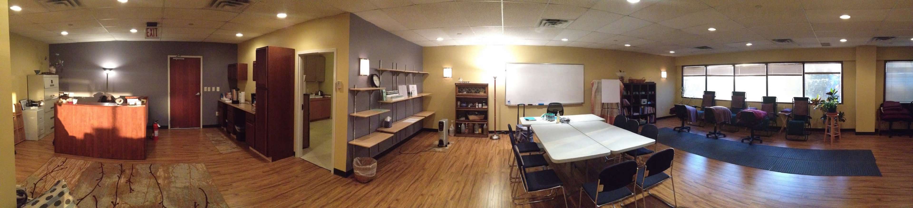 A spacious, well-lit room with a reception area, a large meeting table, and several seating stations arranged along the windows.