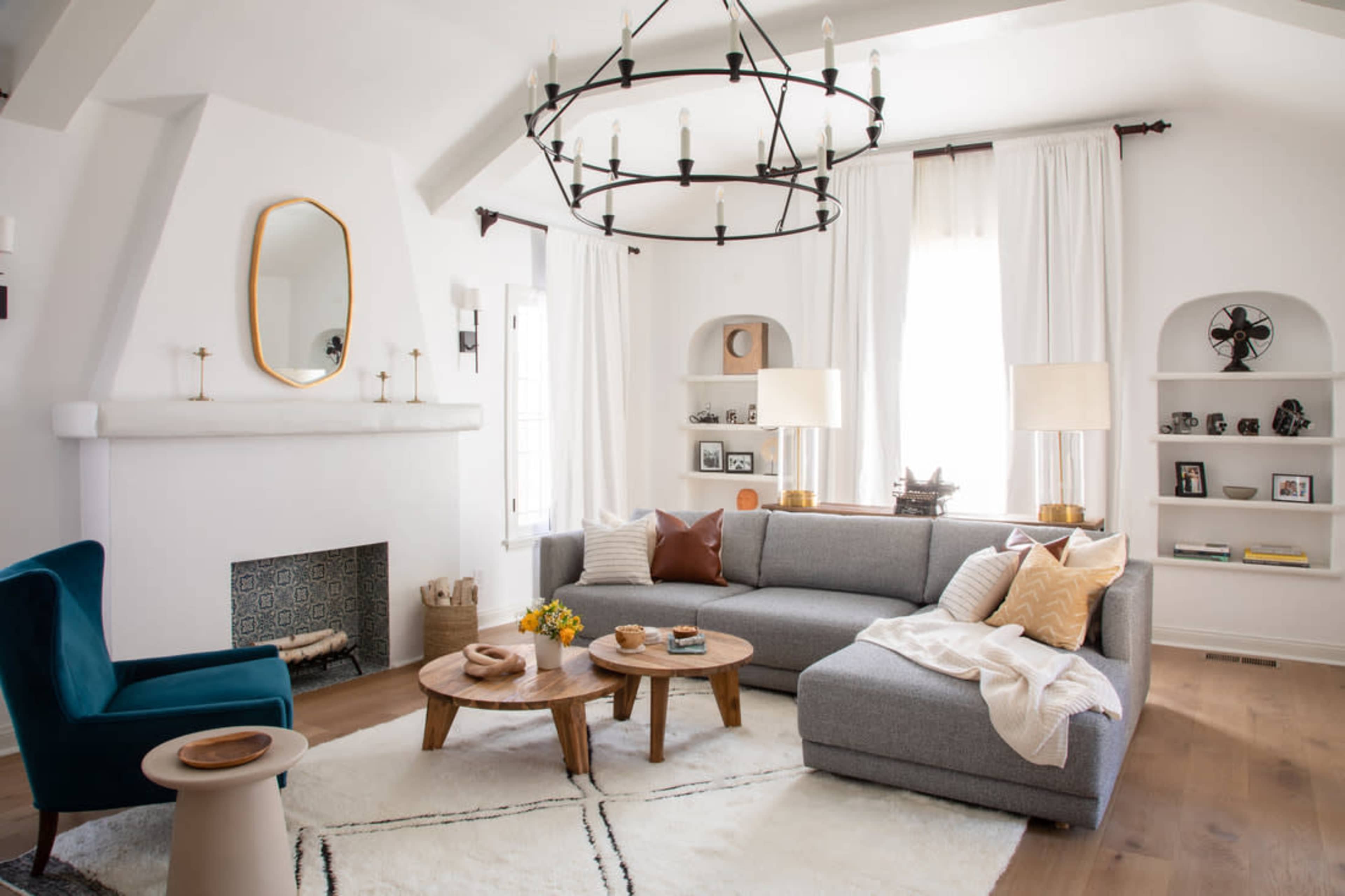 A modern living room features a sectional sofa, a circular wooden coffee table, and built-in shelves, all arranged around a fireplace and illuminated by a large chandelier.