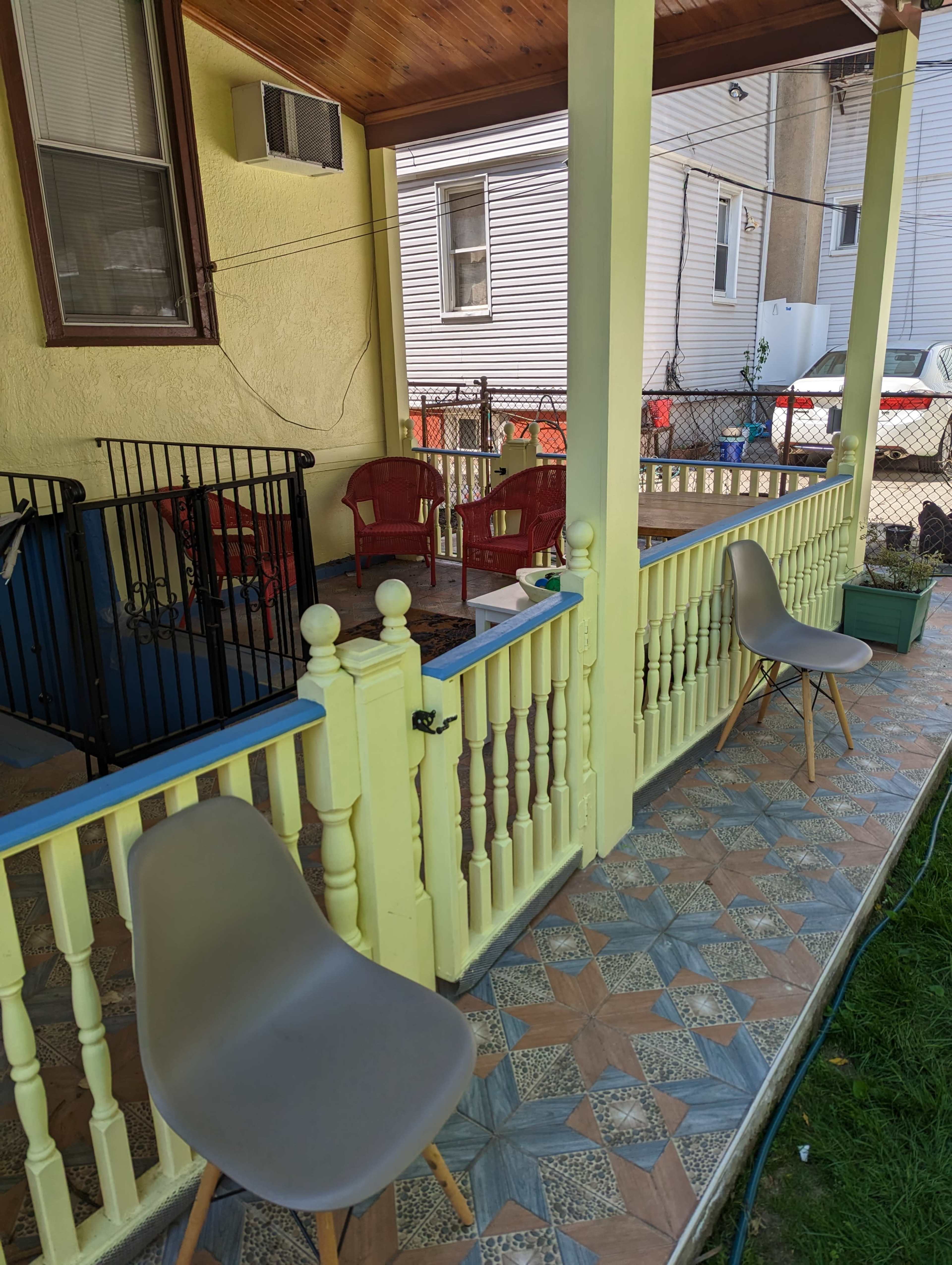 The image shows a porch with two gray chairs, a low railing, and a fenced yard in the background.