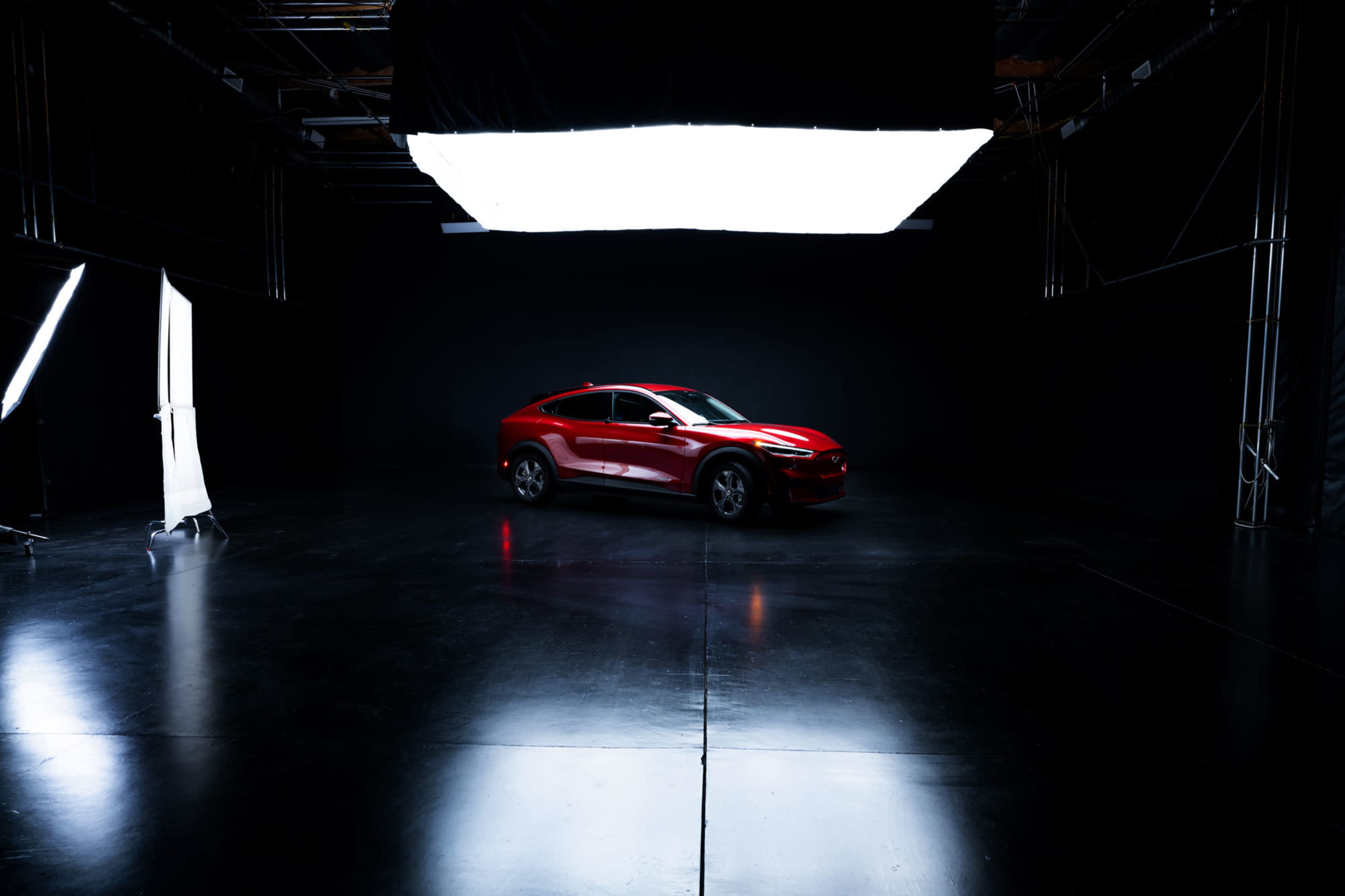 A red car is positioned in a dimly lit studio with a large light source overhead.