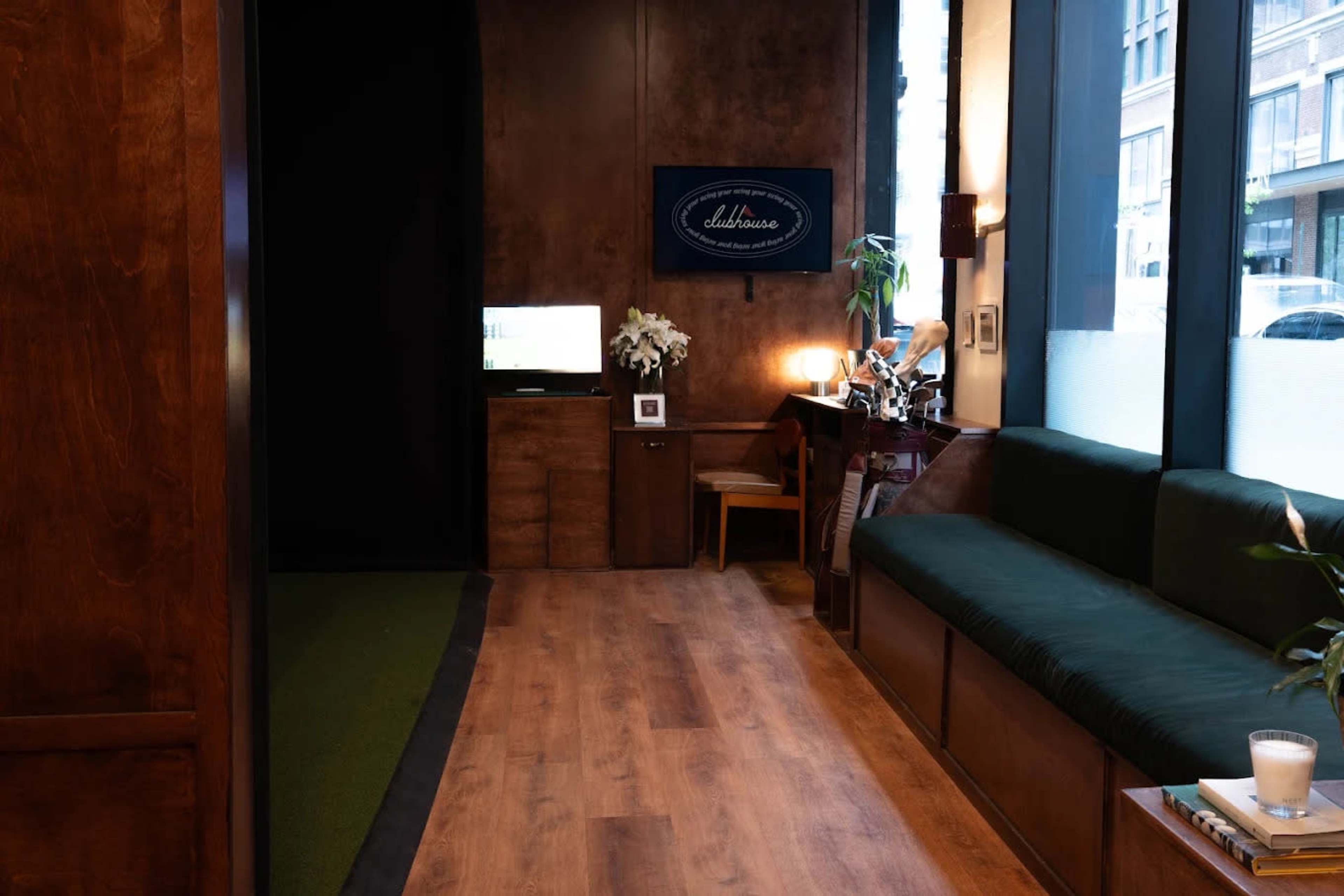 The image shows a modern indoor space featuring wooden paneling, a green carpeted area, a dark couch, and a television mounted on the wall.