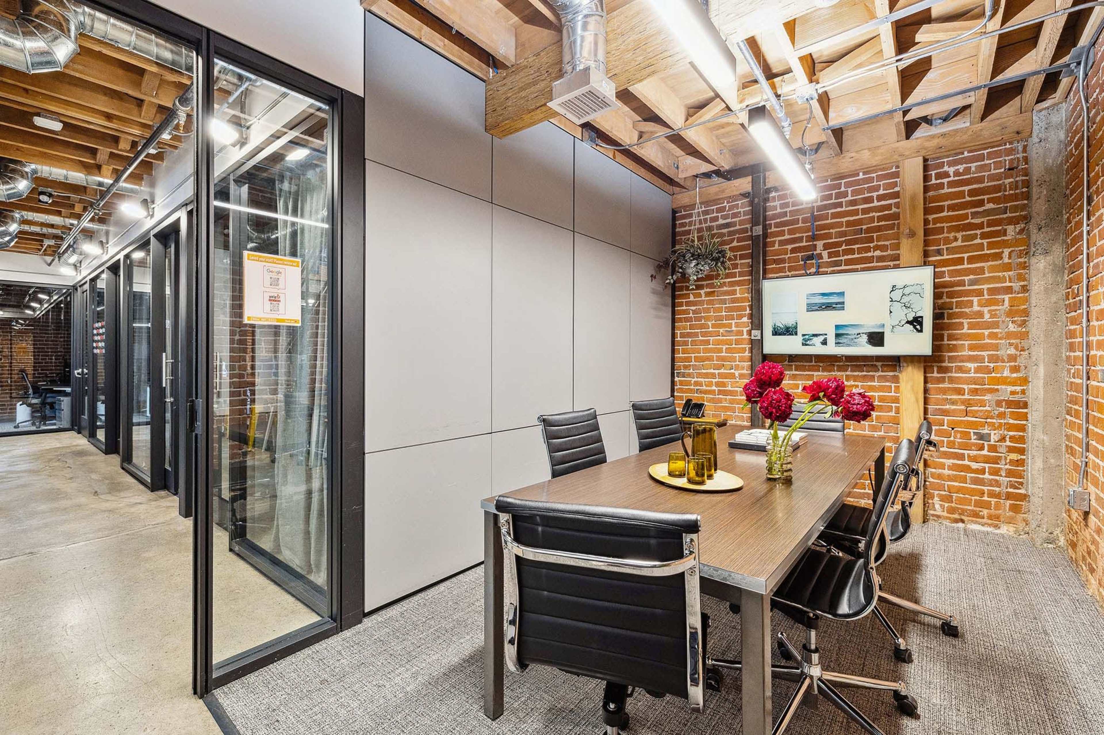 A modern conference room with a wooden table and black chairs is situated among exposed brick walls and industrial ceiling beams.