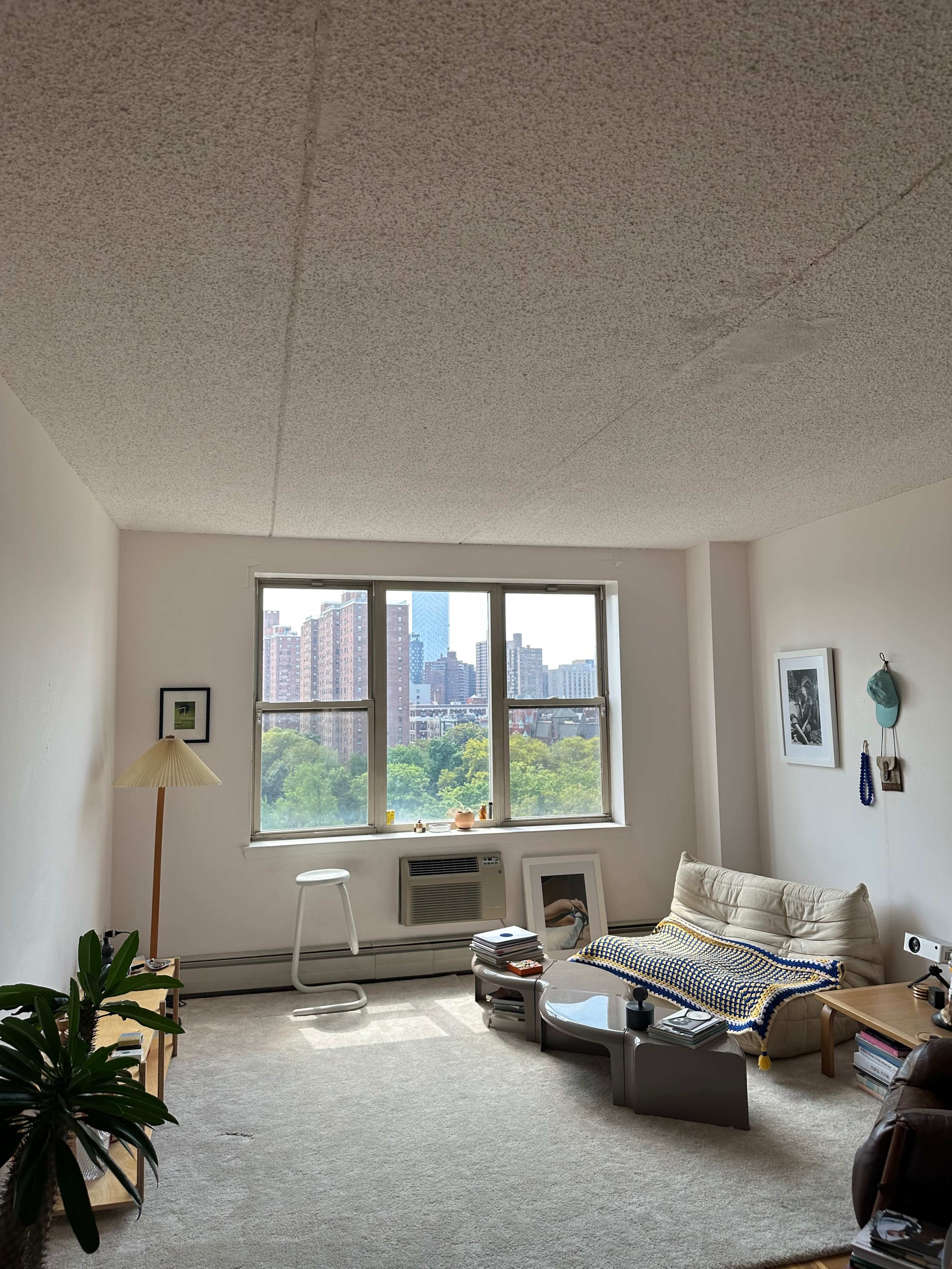 A simple living room with a sofa, coffee table, and a large window revealing a cityscape outside.