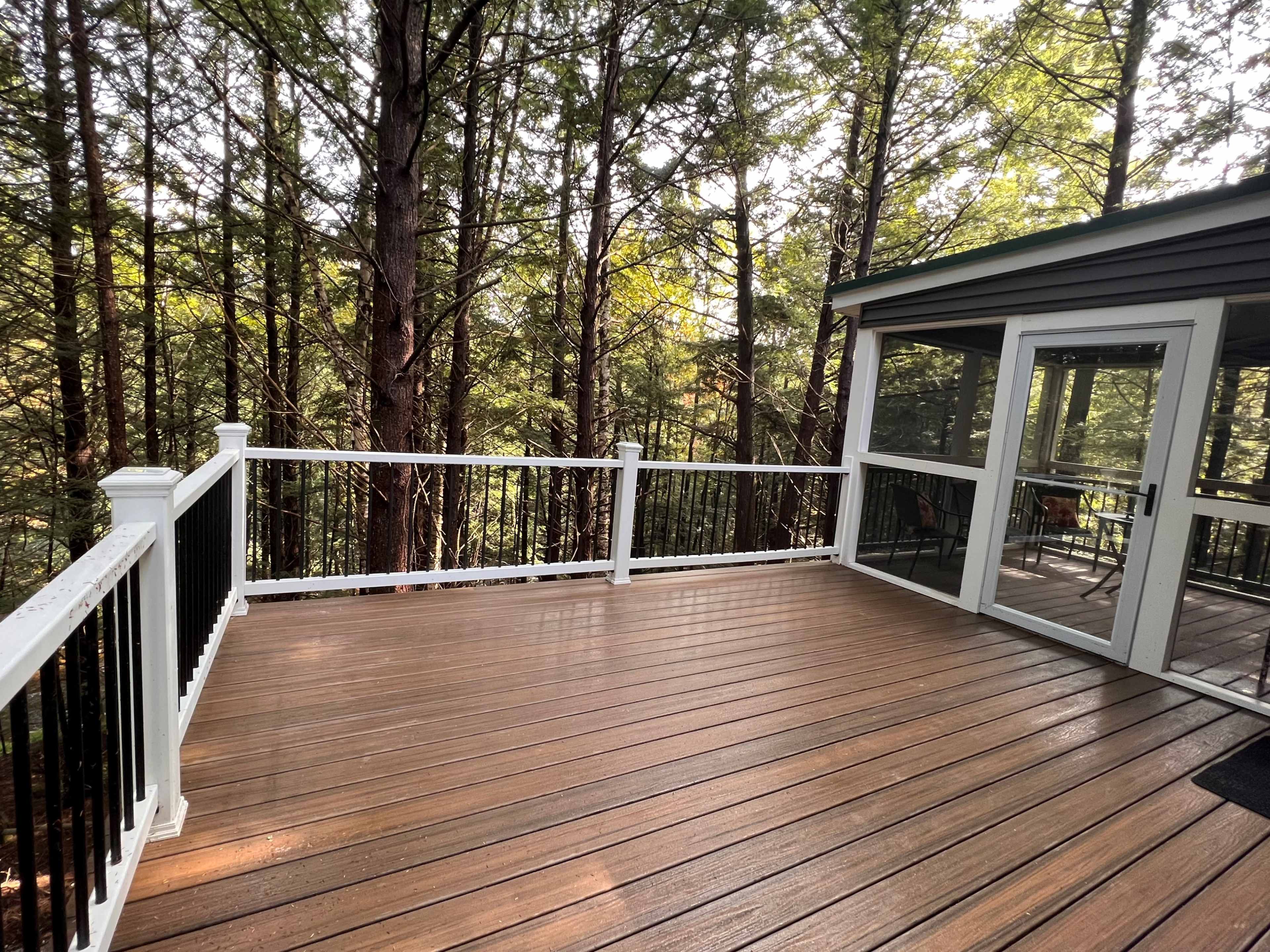 A wooden deck with white railing is surrounded by tall trees in a forested area.
